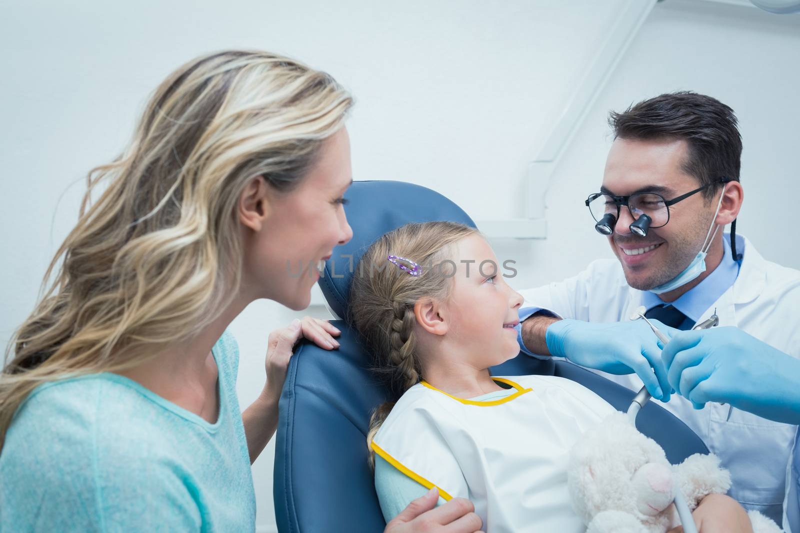 Dentist examining girls teeth in the dentists chair with assistant