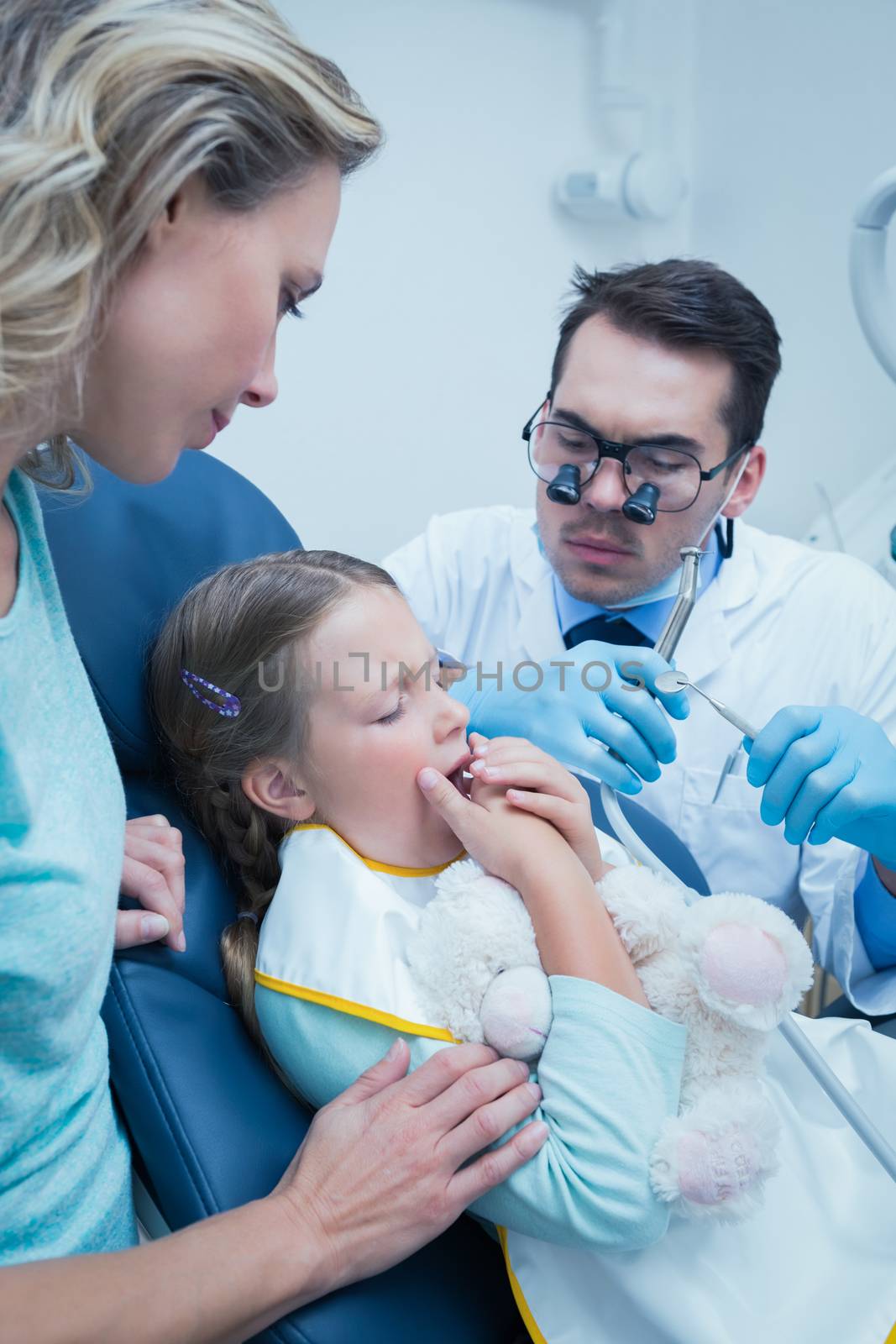 Dentist examining girls teeth in the dentists chair with assistant