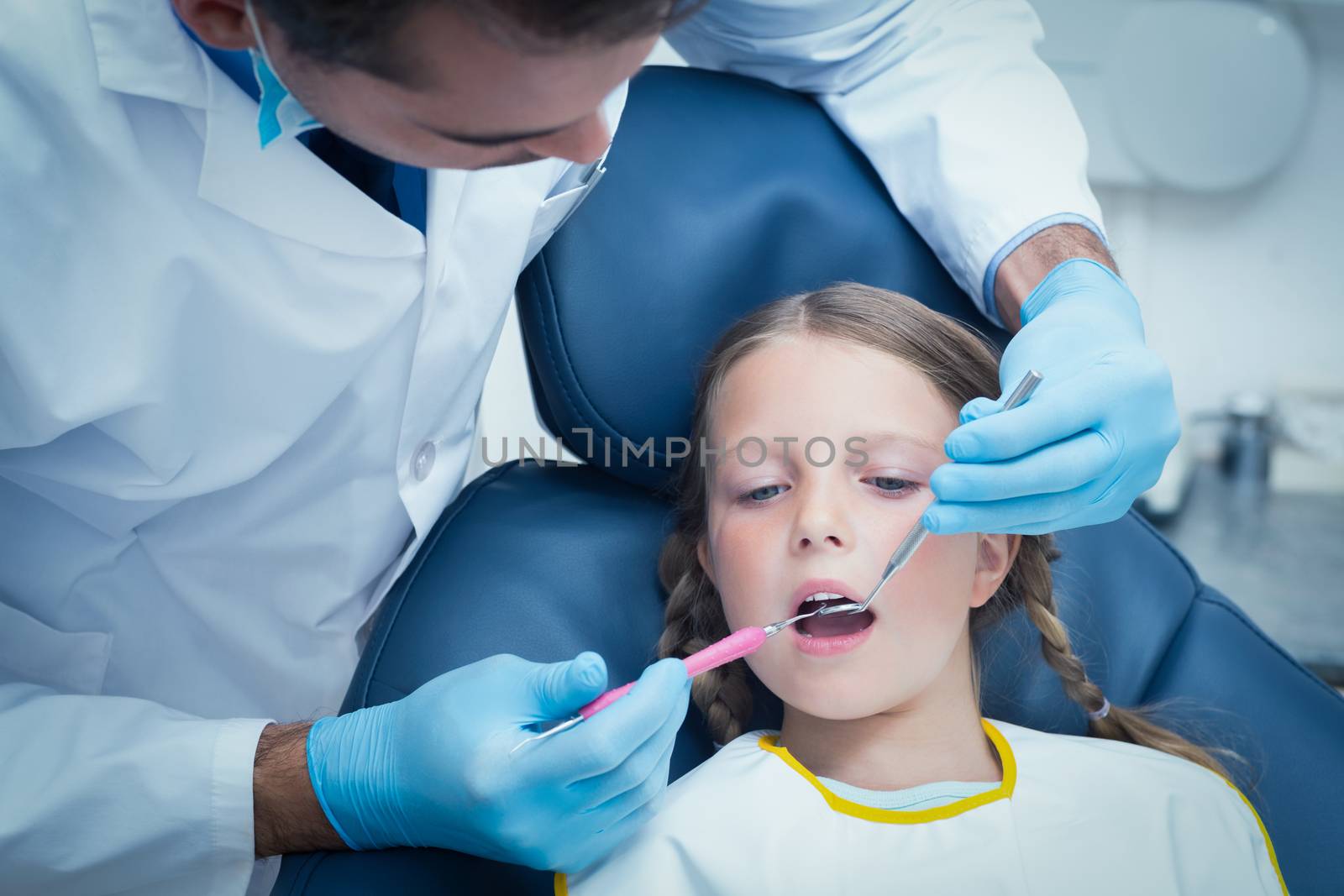 Male dentist examining girls teeth in the dentists chair