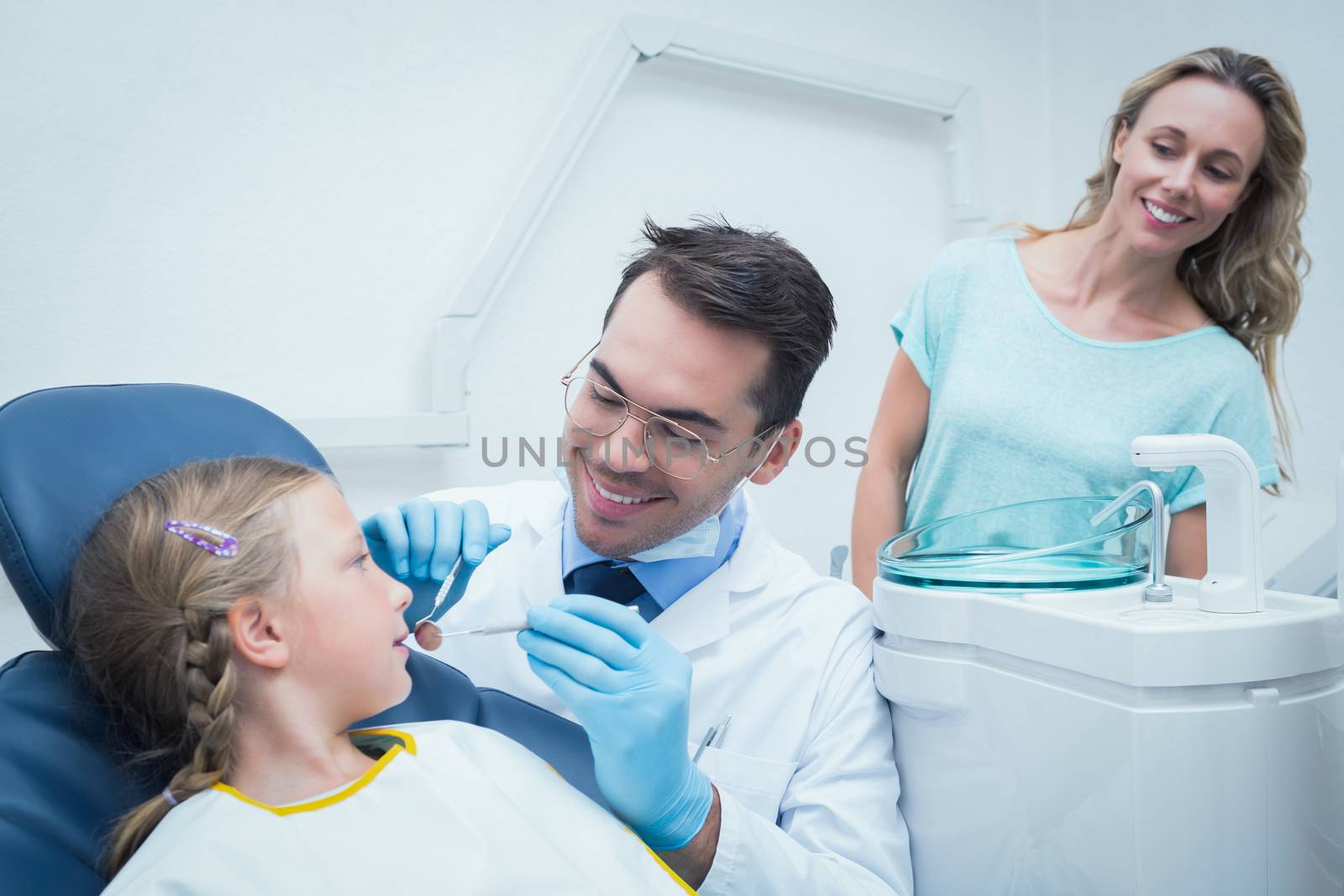 Dentist examining girls teeth in the dentists chair with assistant