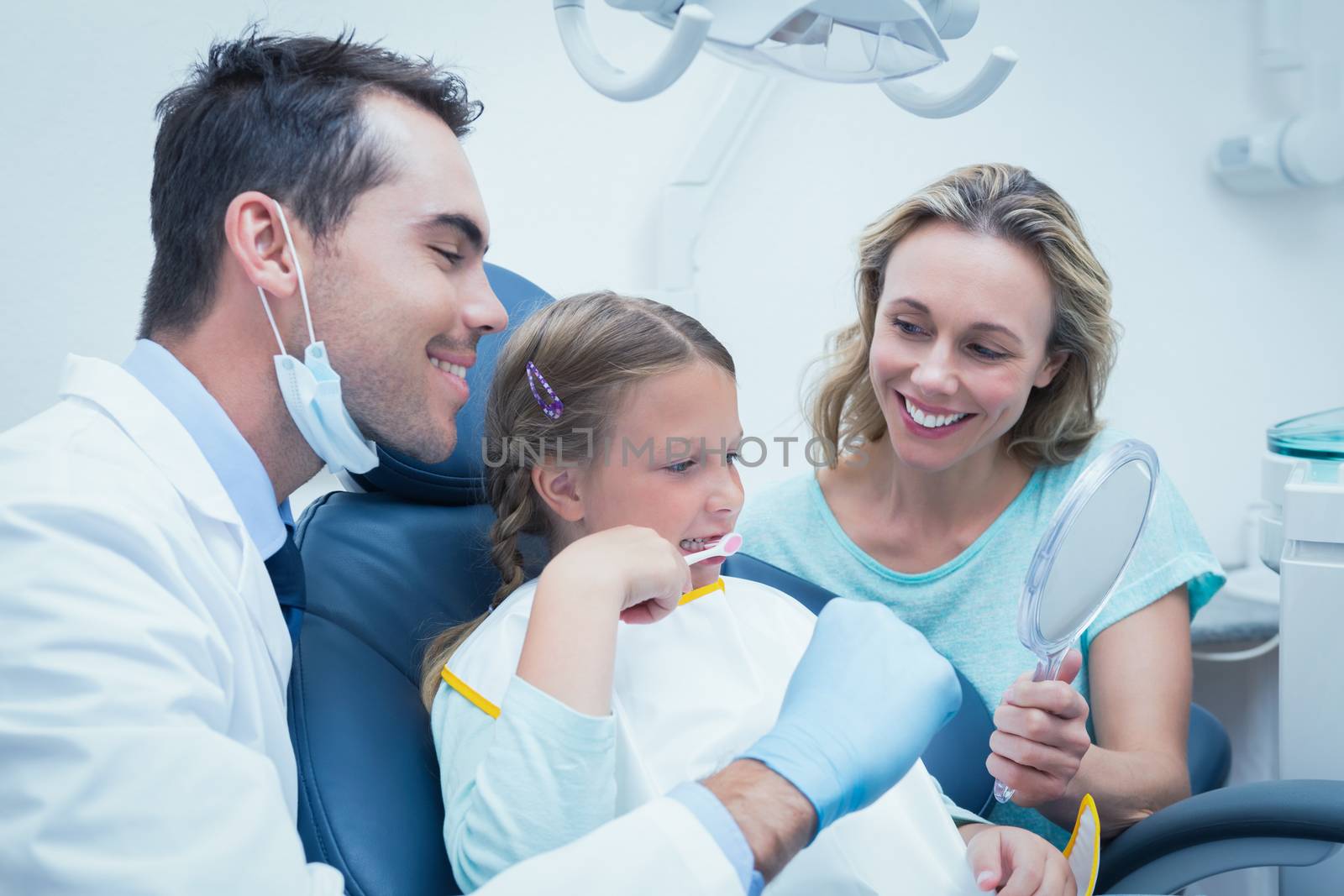 Dentist examining girls teeth in the dentists chair with assistant