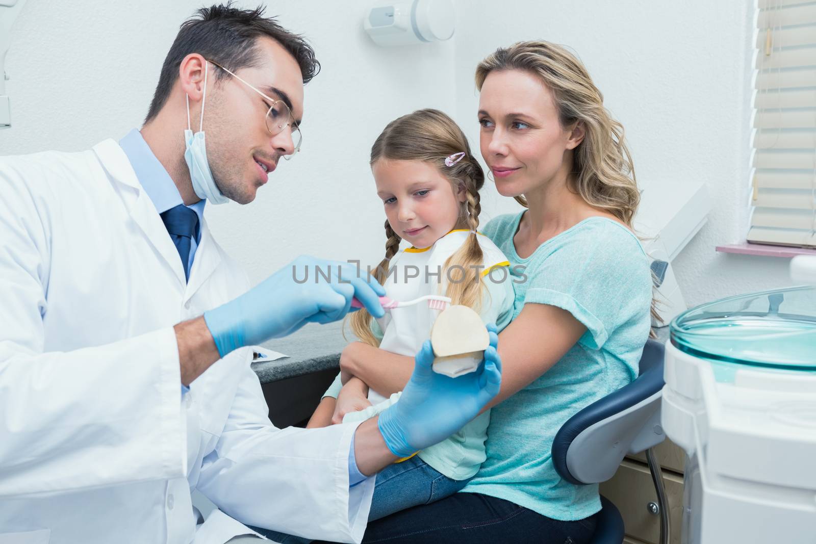 Male dentist with assistant teaching girl how to brush teeth