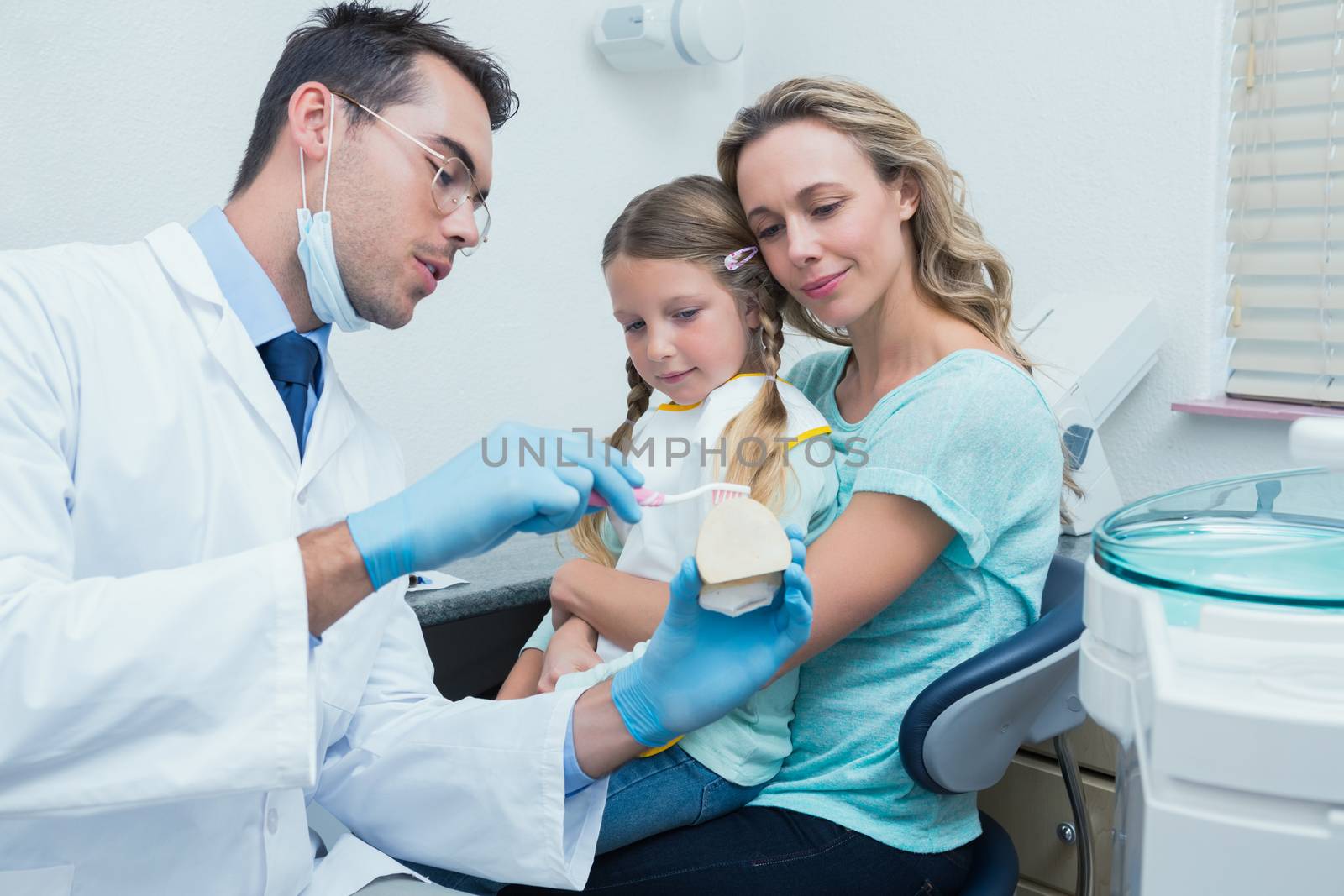 Male dentist with assistant teaching girl how to brush teeth