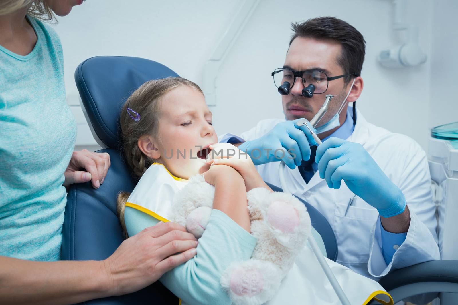 Dentist examining girls teeth in the dentists chair with assistant