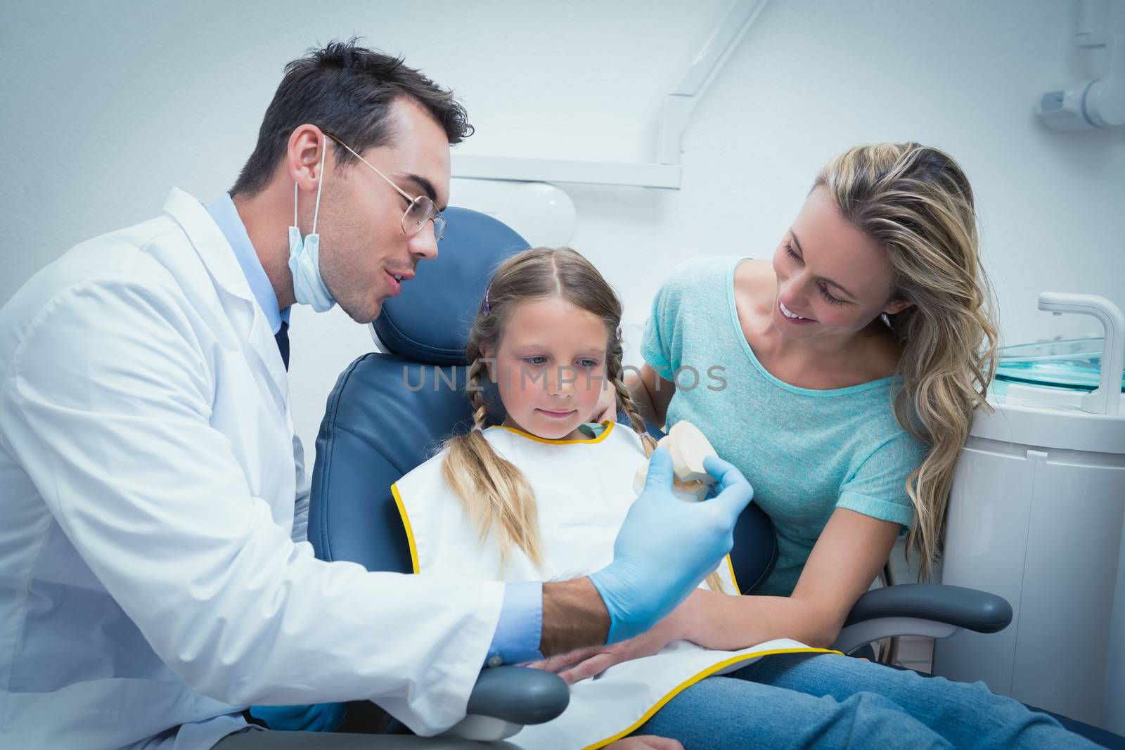Dentist teaching girl how to brush teeth in the dentists chair