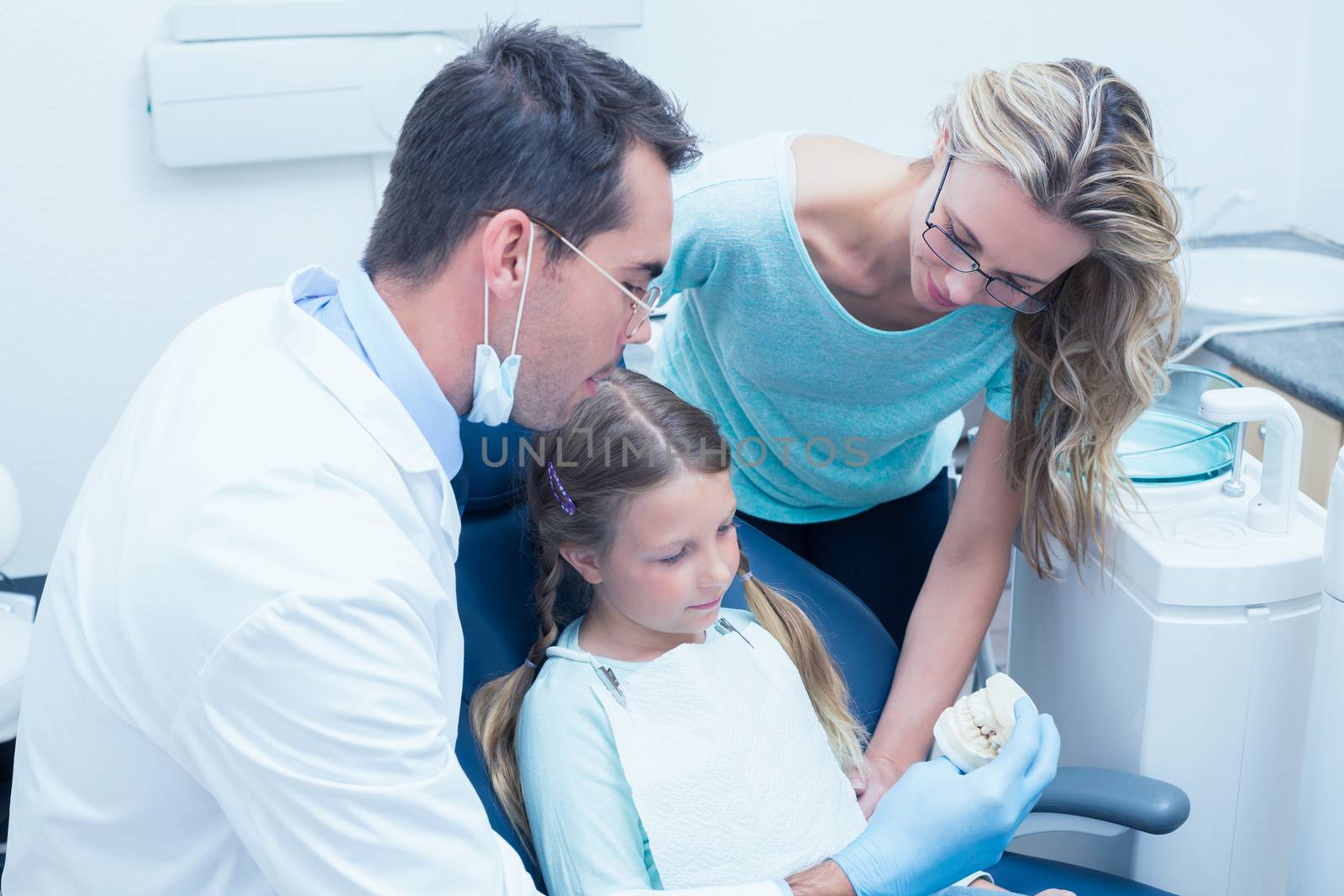 Male dentist with assistant teaching girl how to brush teeth