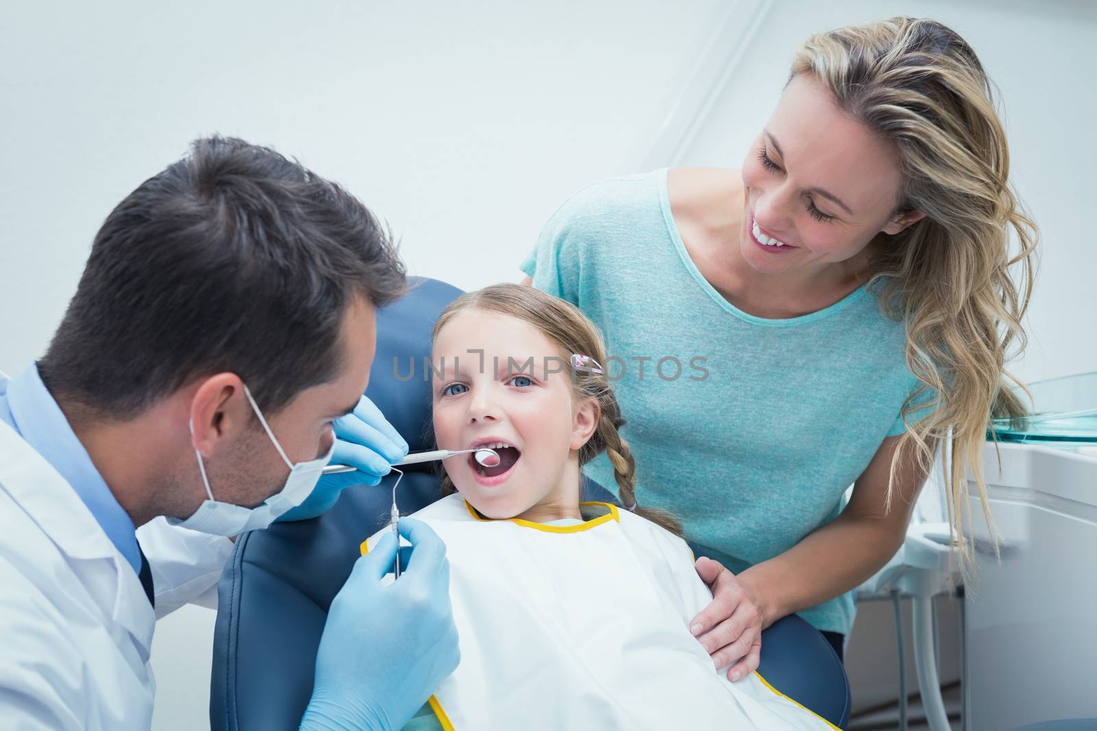 Dentist examining girls teeth in the dentists chair with assistant