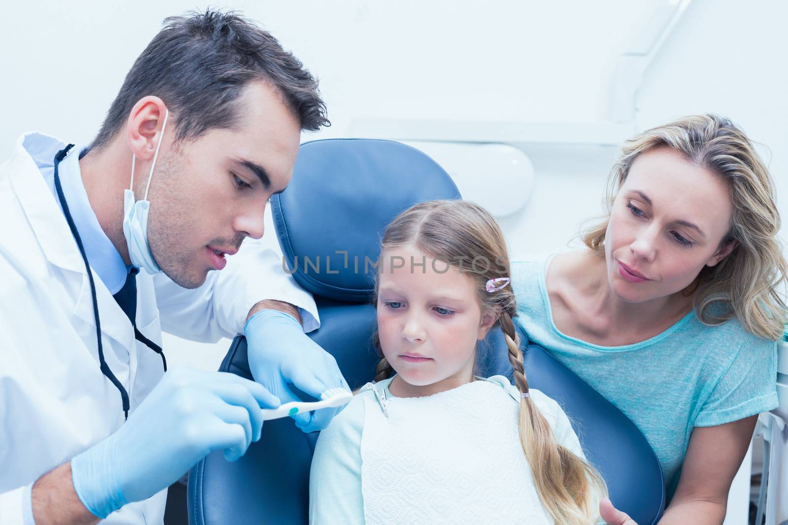 Dentist with assistant teaching girl how to brush teeth by Wavebreakmedia