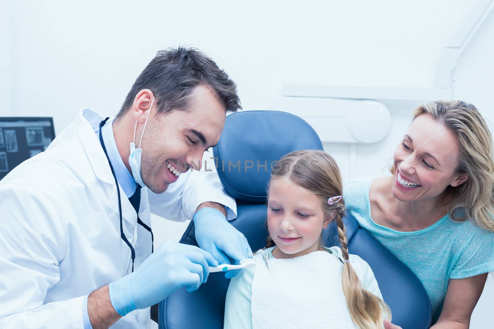 Male dentist with assistant teaching girl how to brush teeth