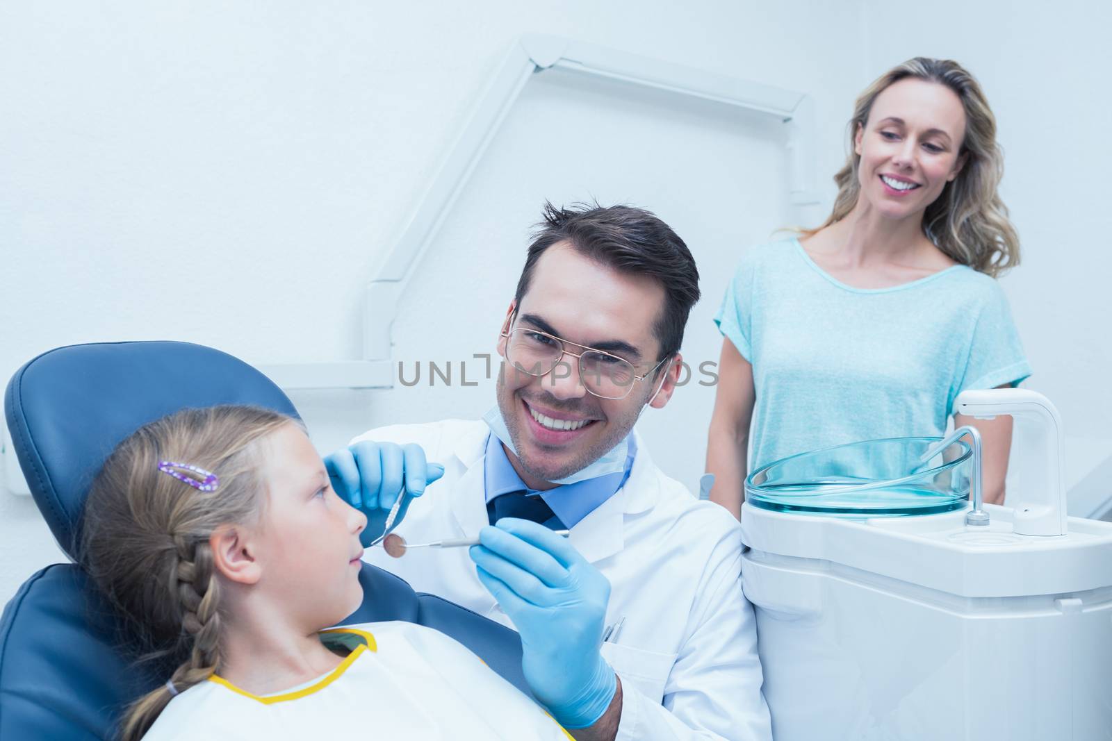 Dentist examining girls teeth in the dentists chair with assistant