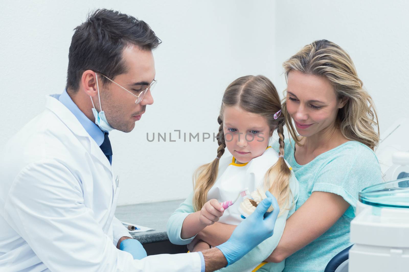 Dentist with assistant teaching girl how to brush teeth by Wavebreakmedia
