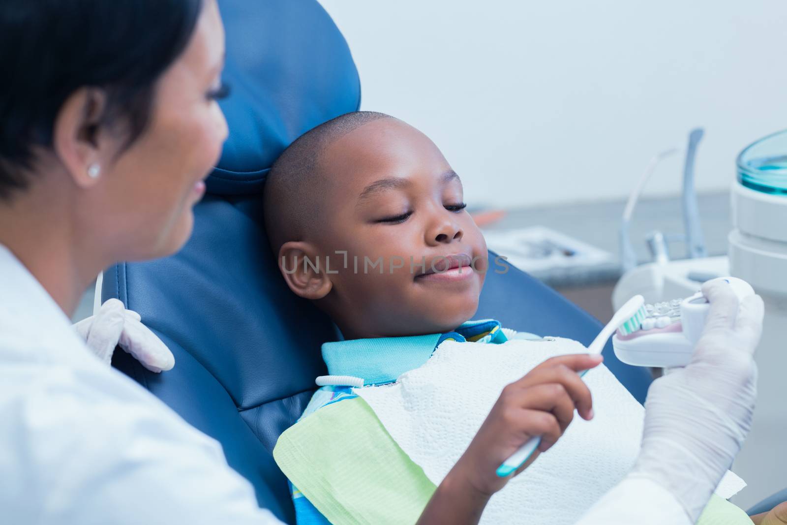 Female dentist teaching boy how to brush teeth by Wavebreakmedia