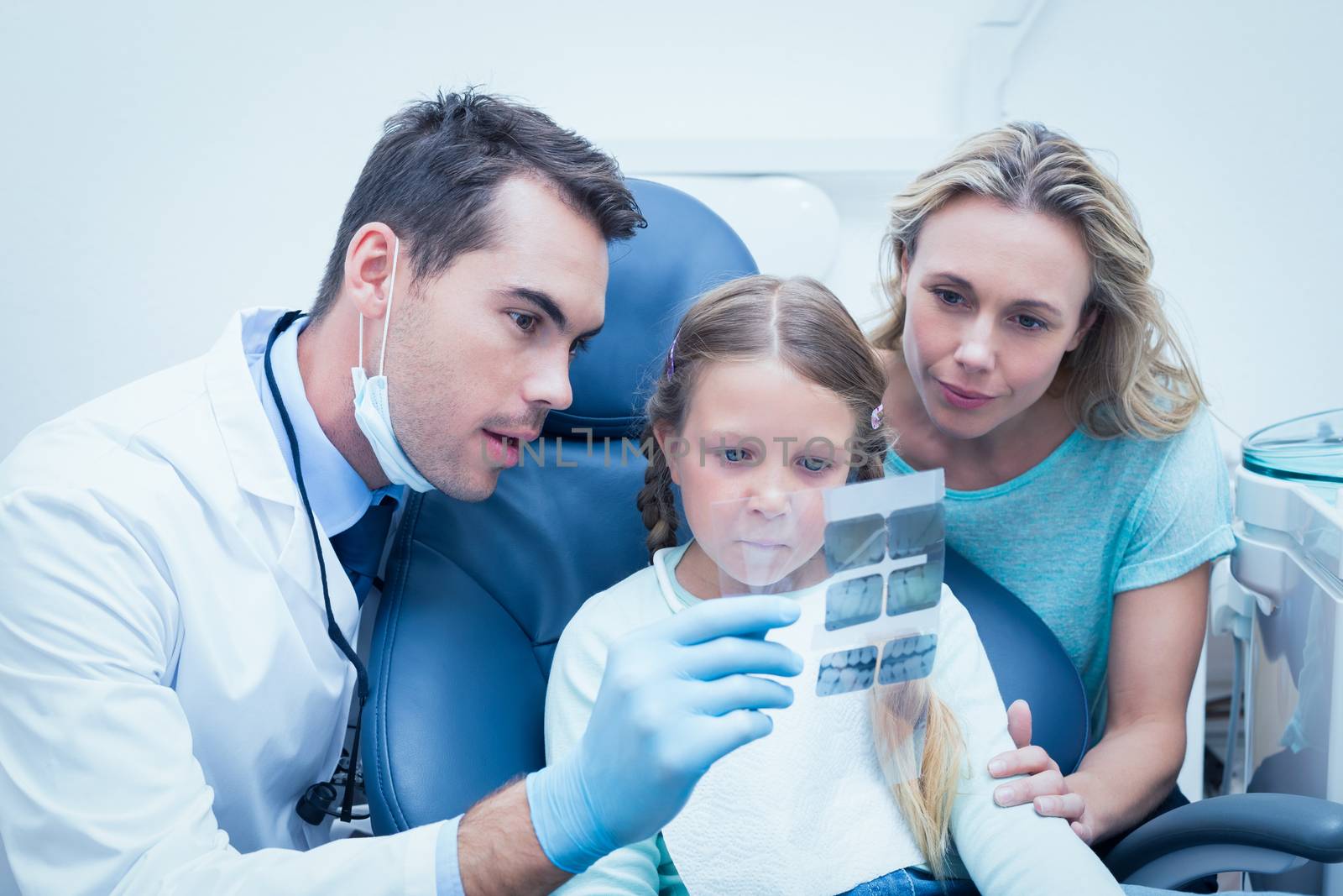 Male dentist with assistant showing little girl her mouth x-ray