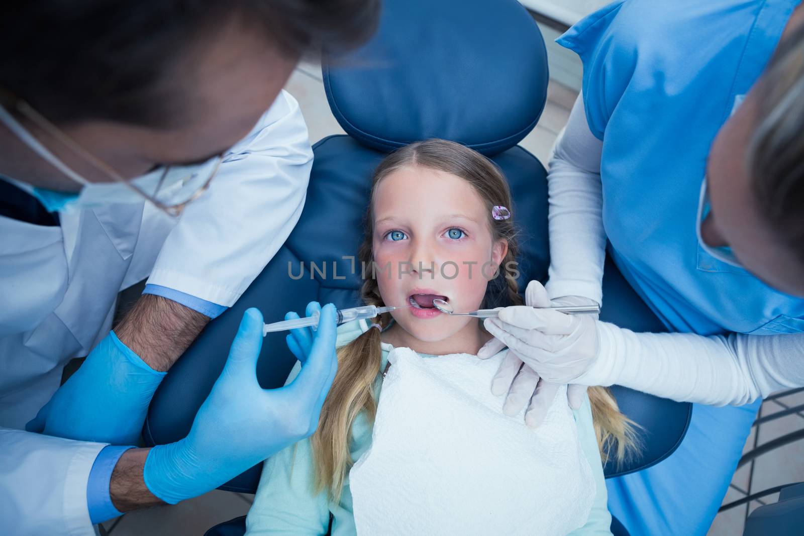 Dentist with assistant examining girls teeth in the dentists chair