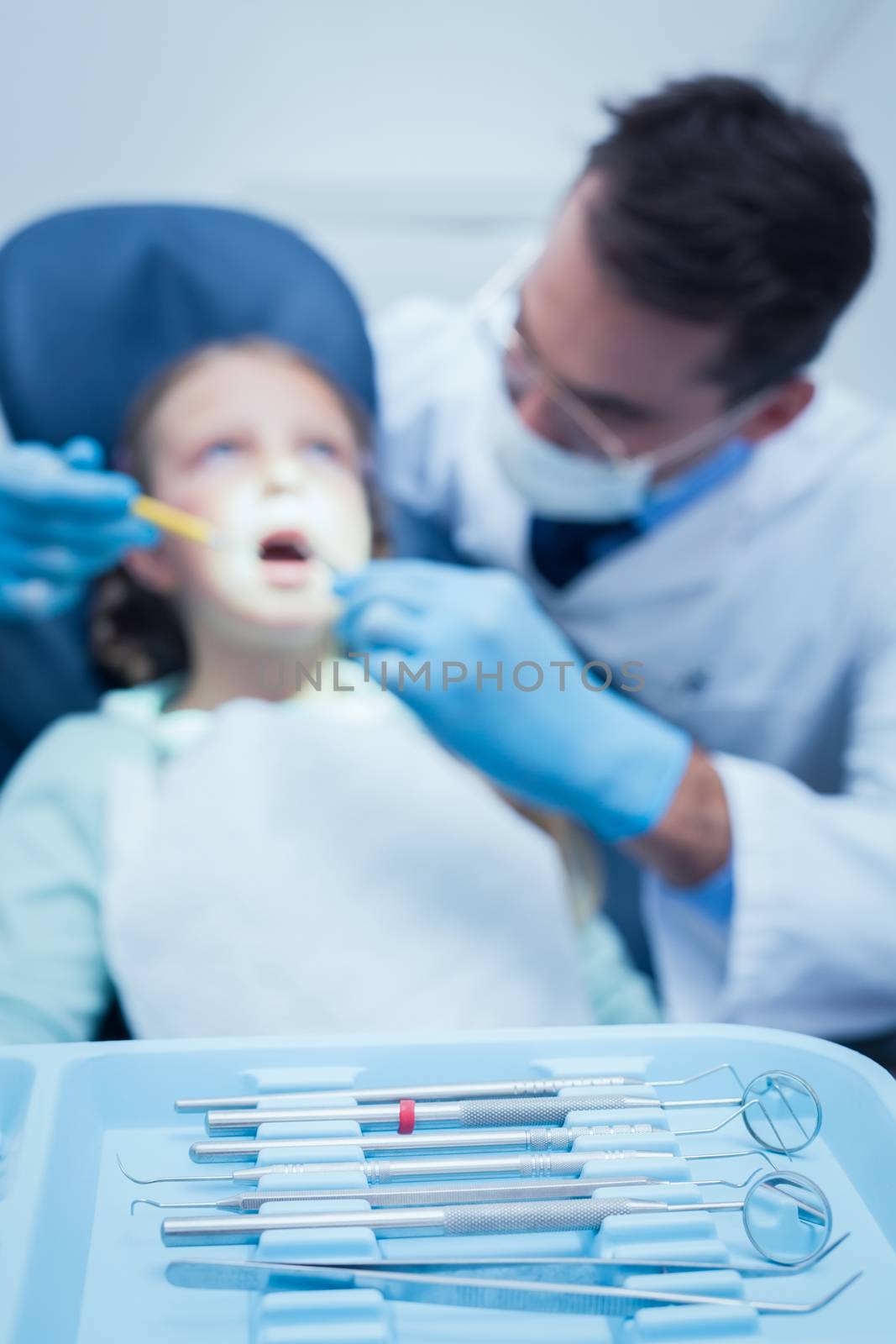 Male dentist examining girls teeth in the dentists chair