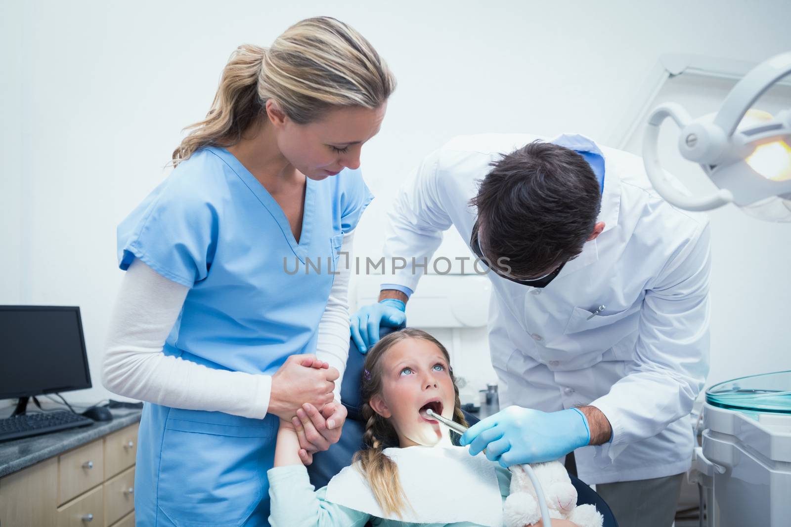 Dentist with assistant examining girls teeth in the dentists chair