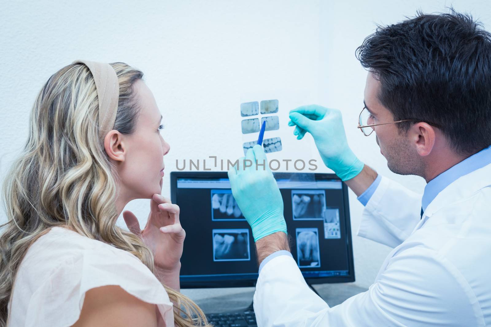 Side view of male dentist showing woman her mouth x-ray