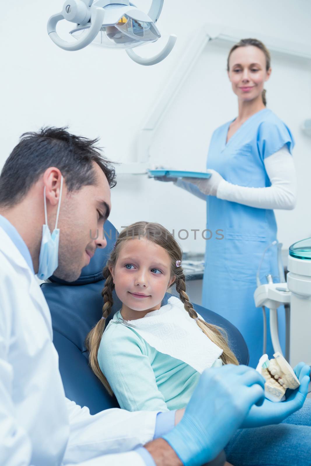 Male dentist teaching girl how to brush teeth in the dentists chair