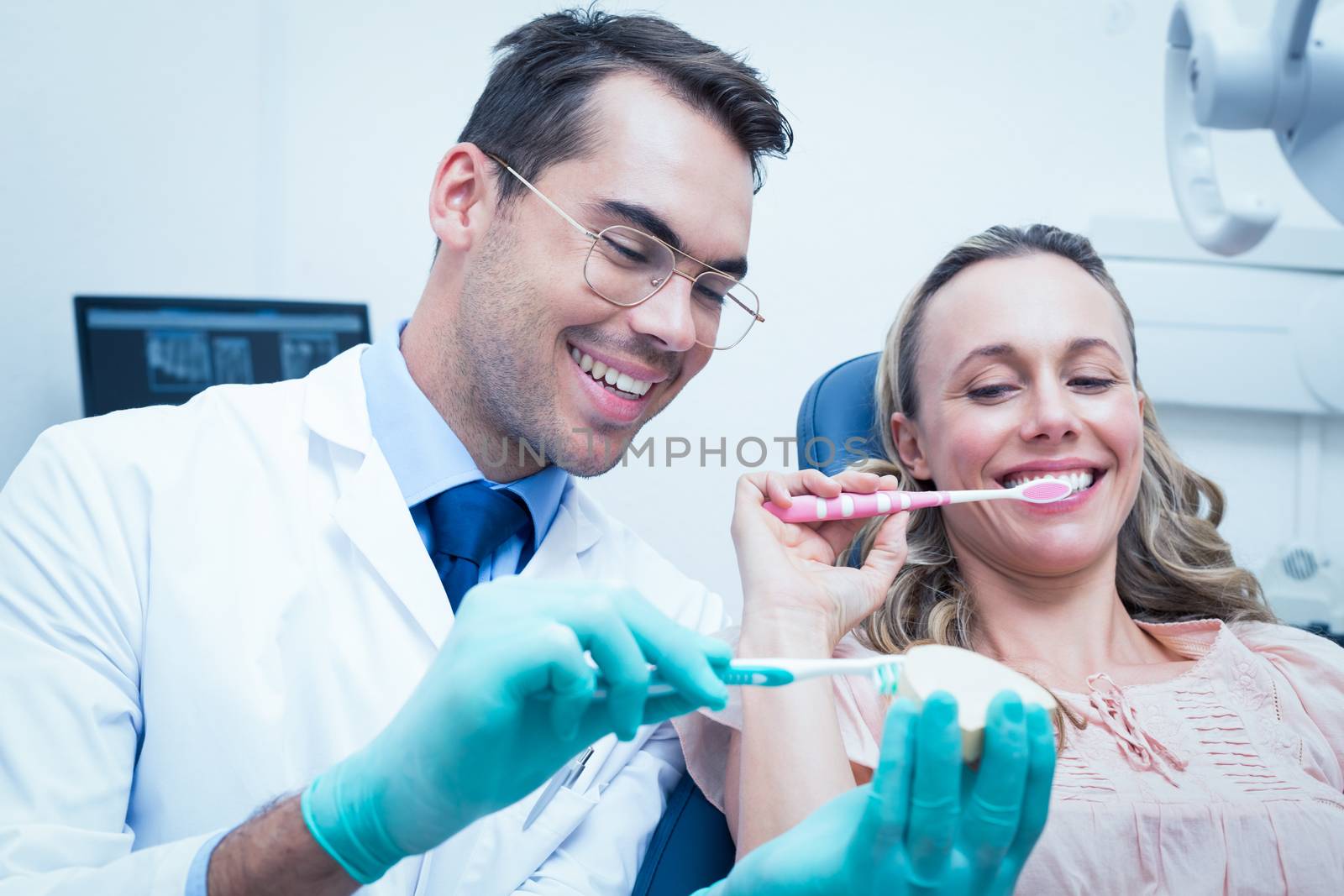 Male dentist teaching woman how to brush teeth by Wavebreakmedia