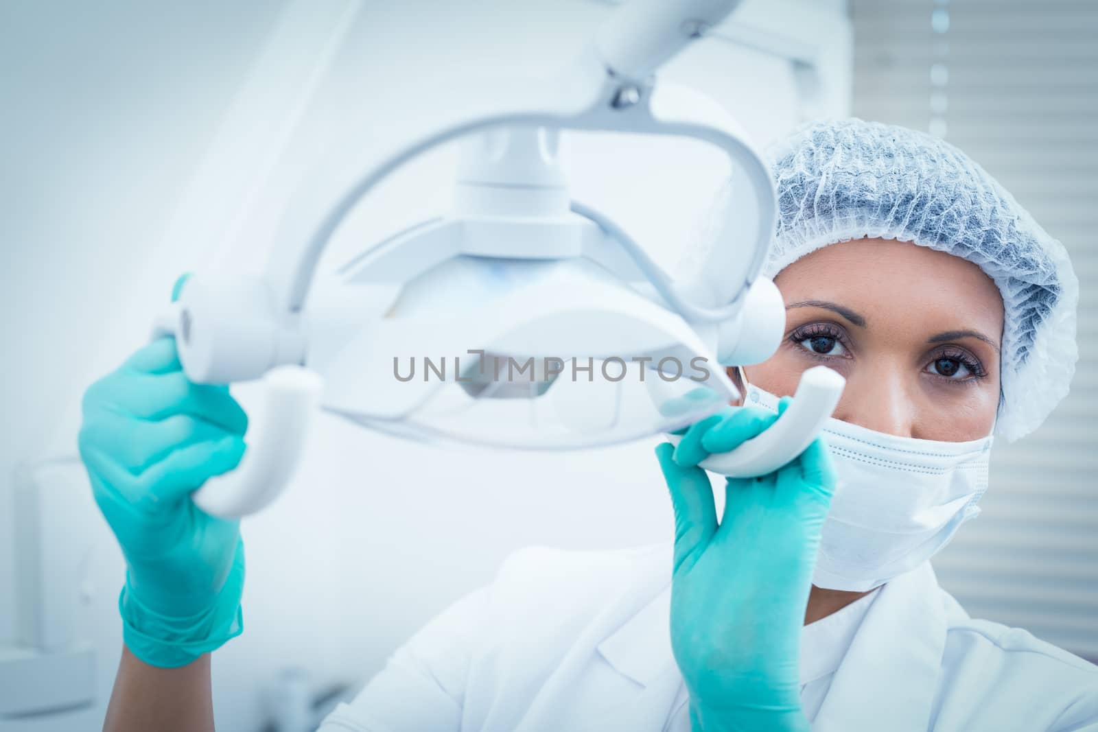Portrait of female dentist in surgical mask adjusting light