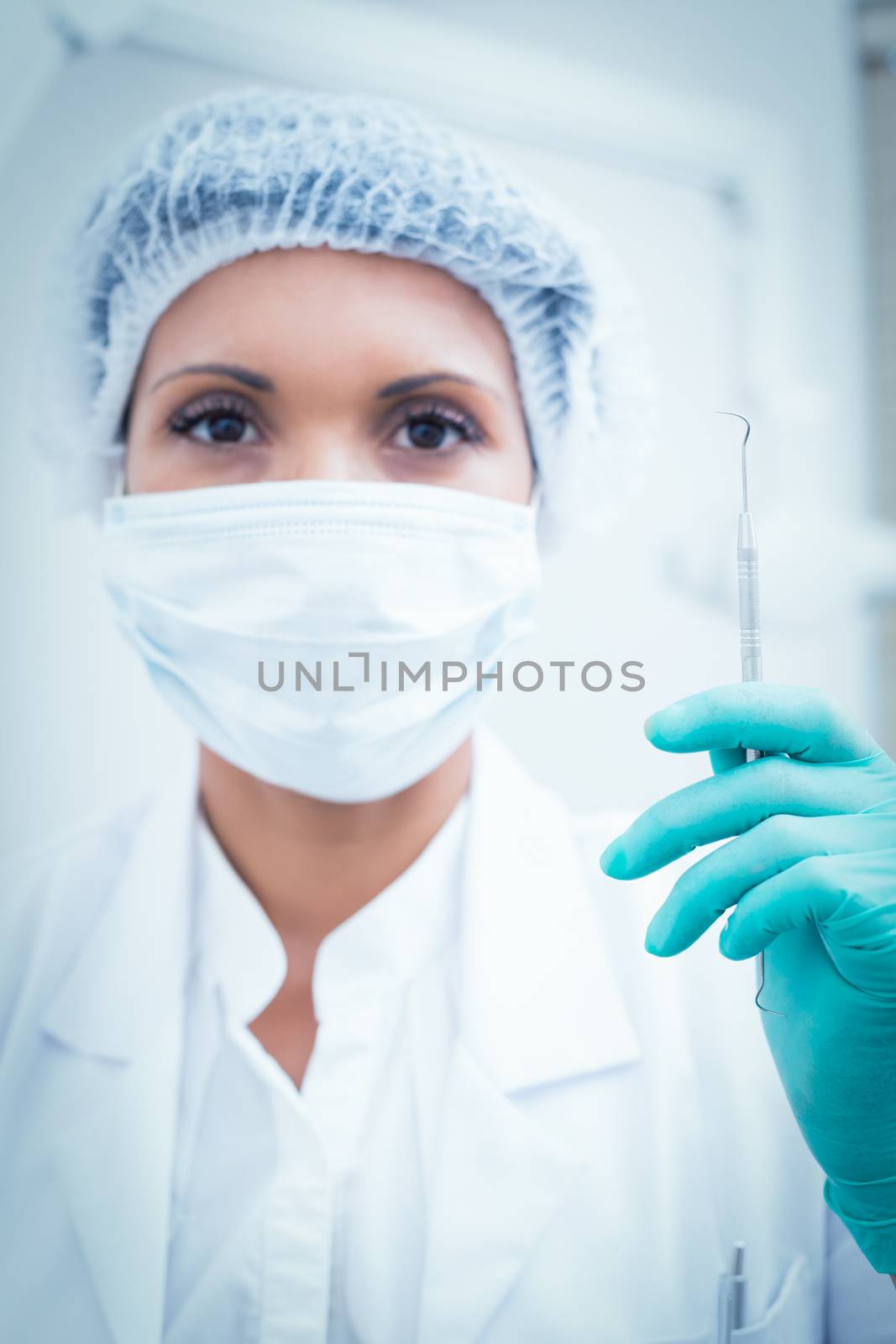 Portrait of female dentist in surgical mask holding hook