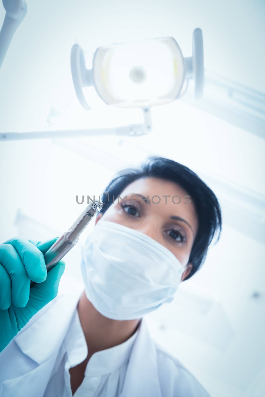 Low angle view of female dentist in surgical mask holding dental drill