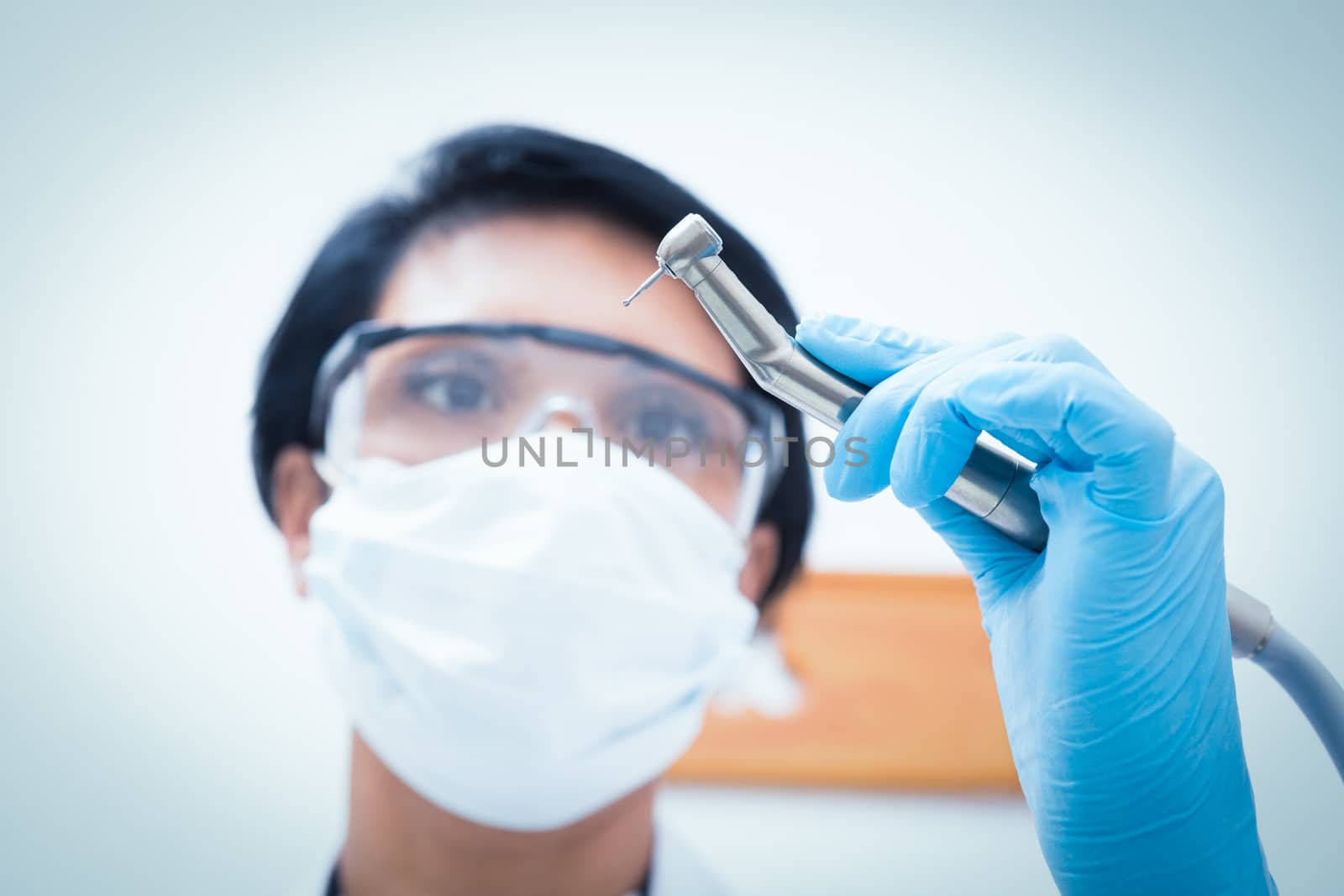 Female dentist in surgical mask holding dental drill by Wavebreakmedia