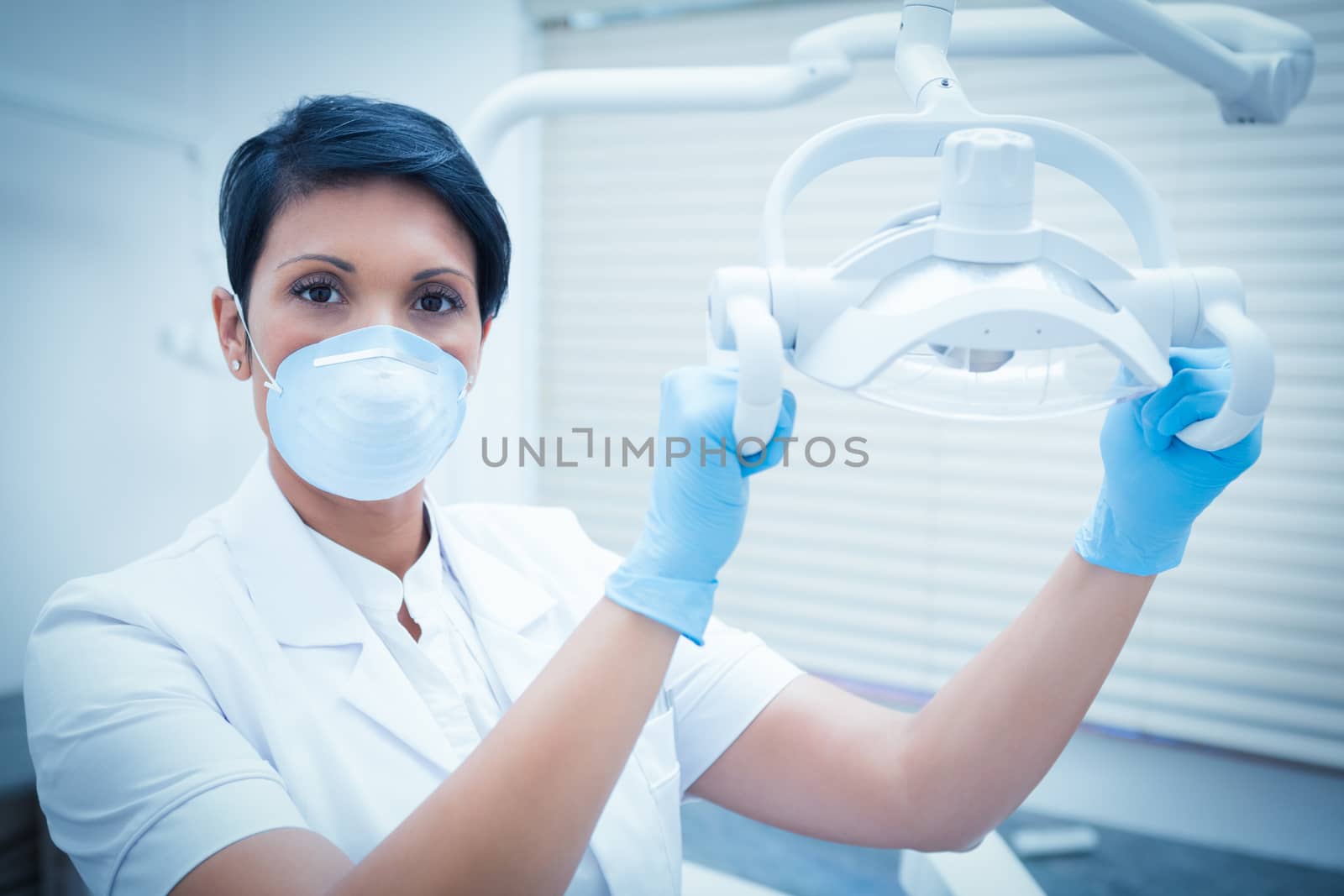 Demale dentist in surgical mask adjusting light by Wavebreakmedia
