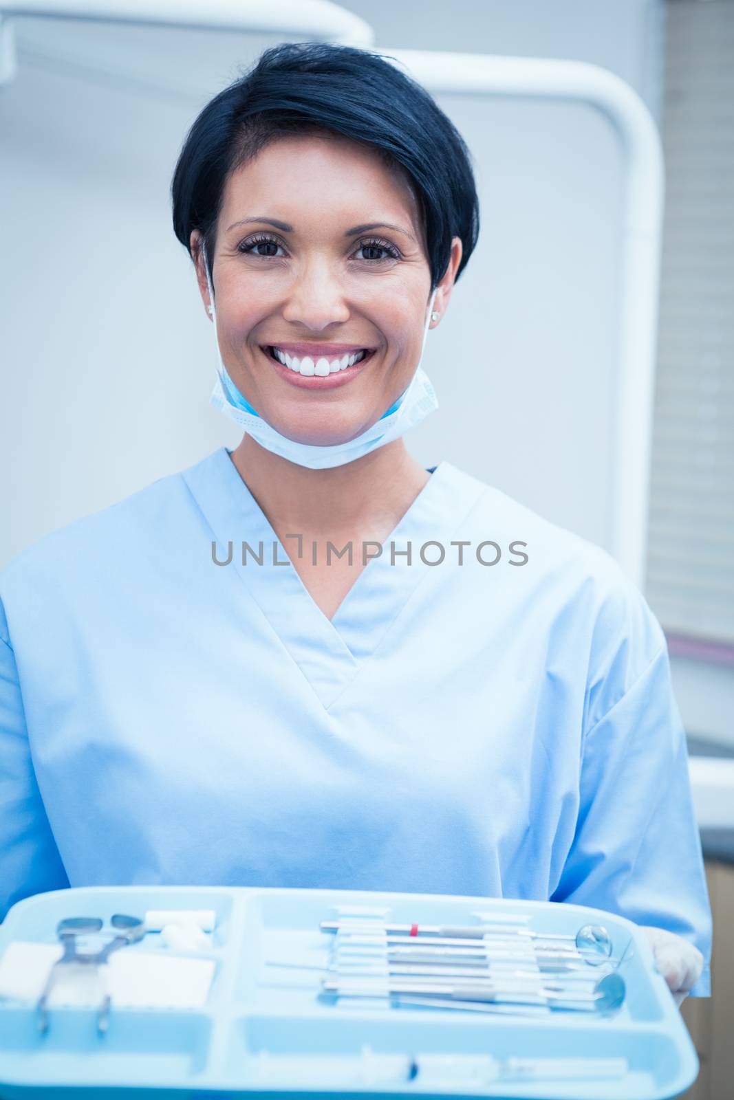 Female dentist in blue scrubs holding tray of tools by Wavebreakmedia