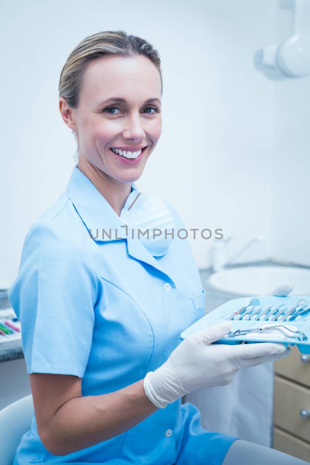 Female dentist in blue scrubs holding tray of tools by Wavebreakmedia