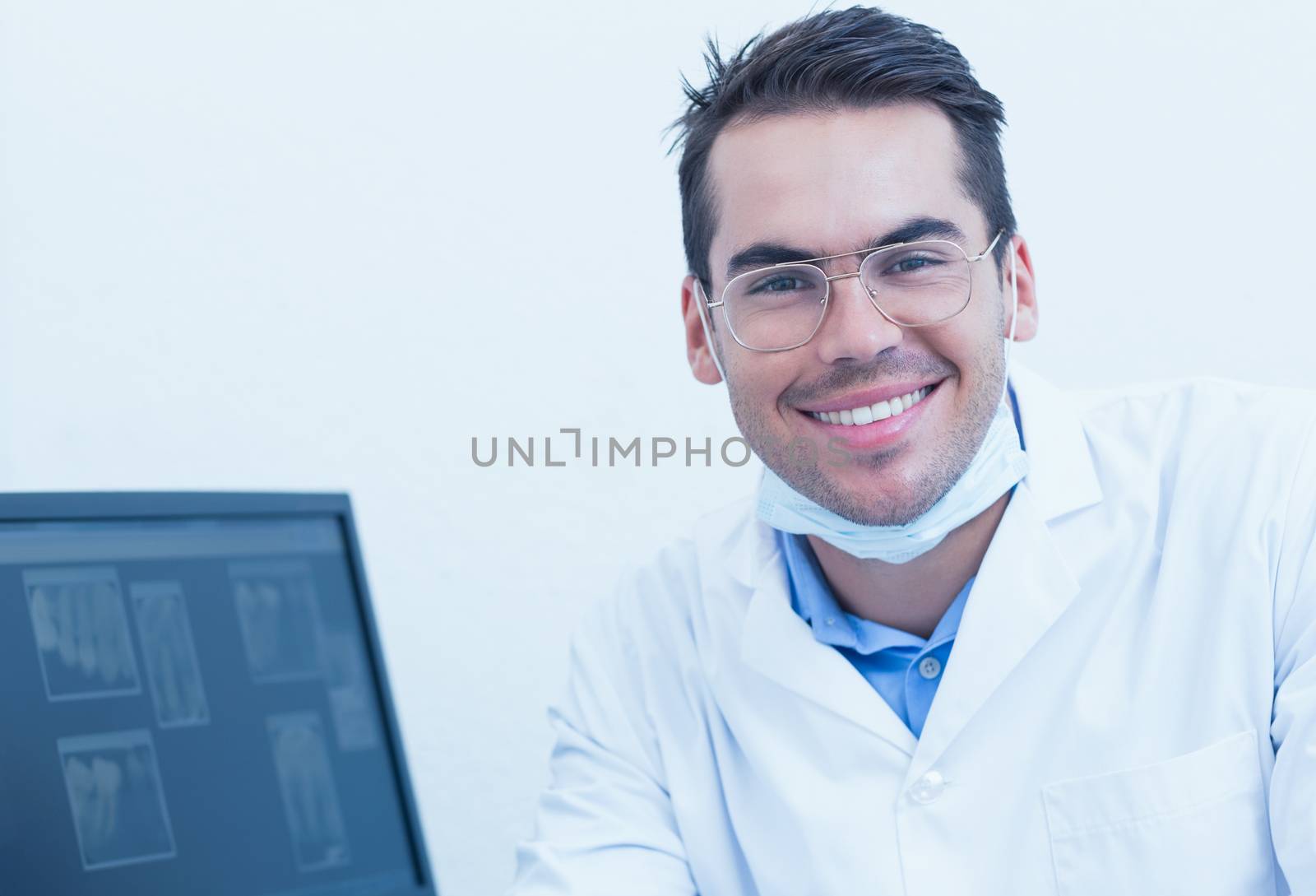 Portrait of smiling male dentist with computer monitor