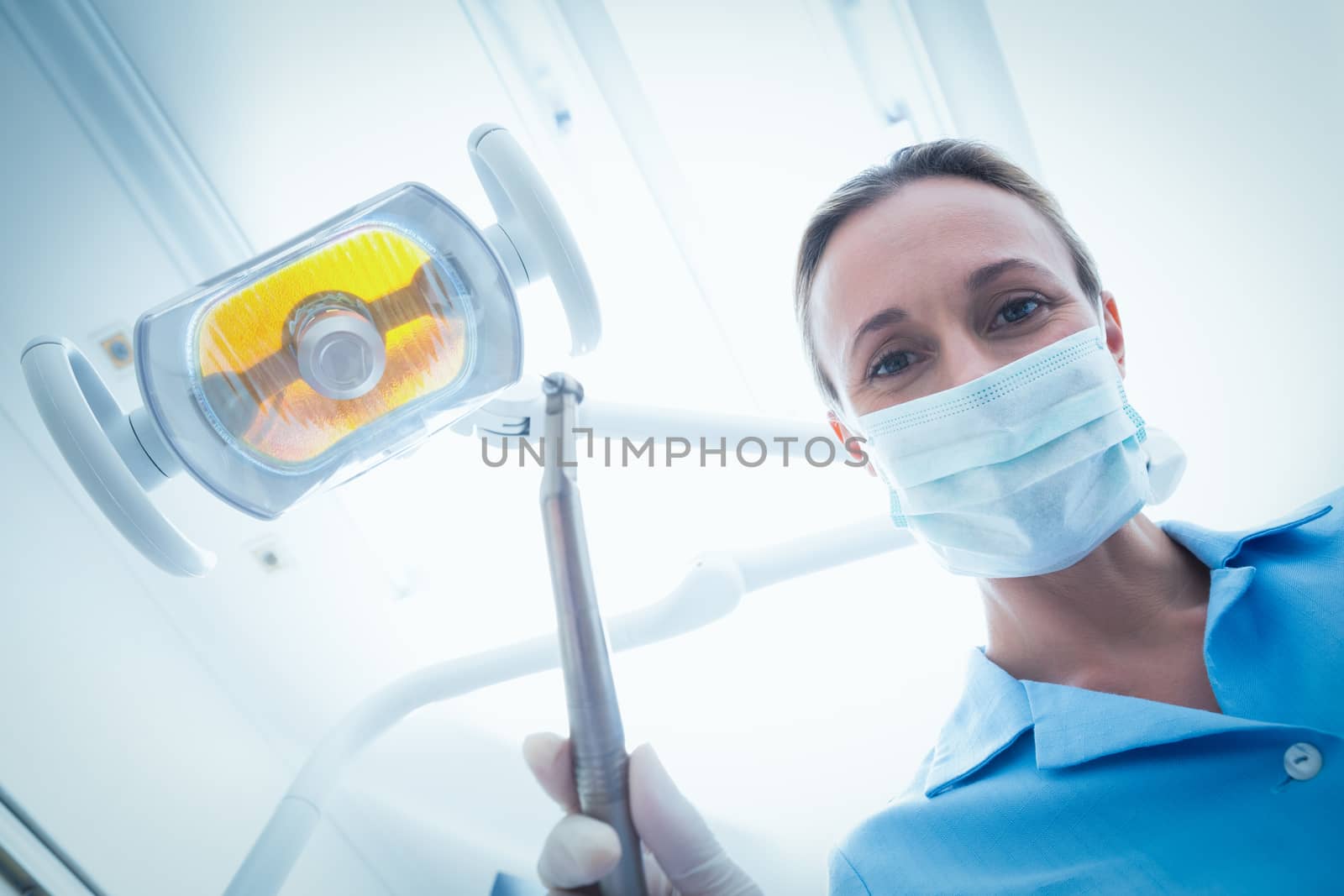 Low angle portrait of female dentist in surgical mask holding dental tool