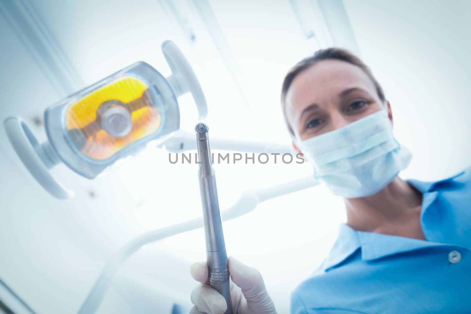 Low angle portrait of female dentist in surgical mask holding dental tool