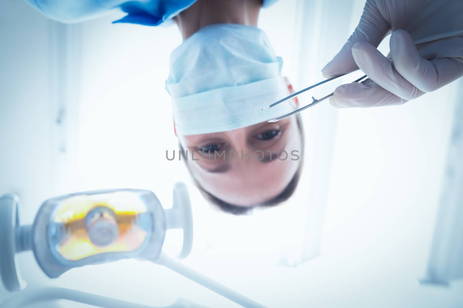 Low angle portrait of female dentist in surgical mask holding dental tool