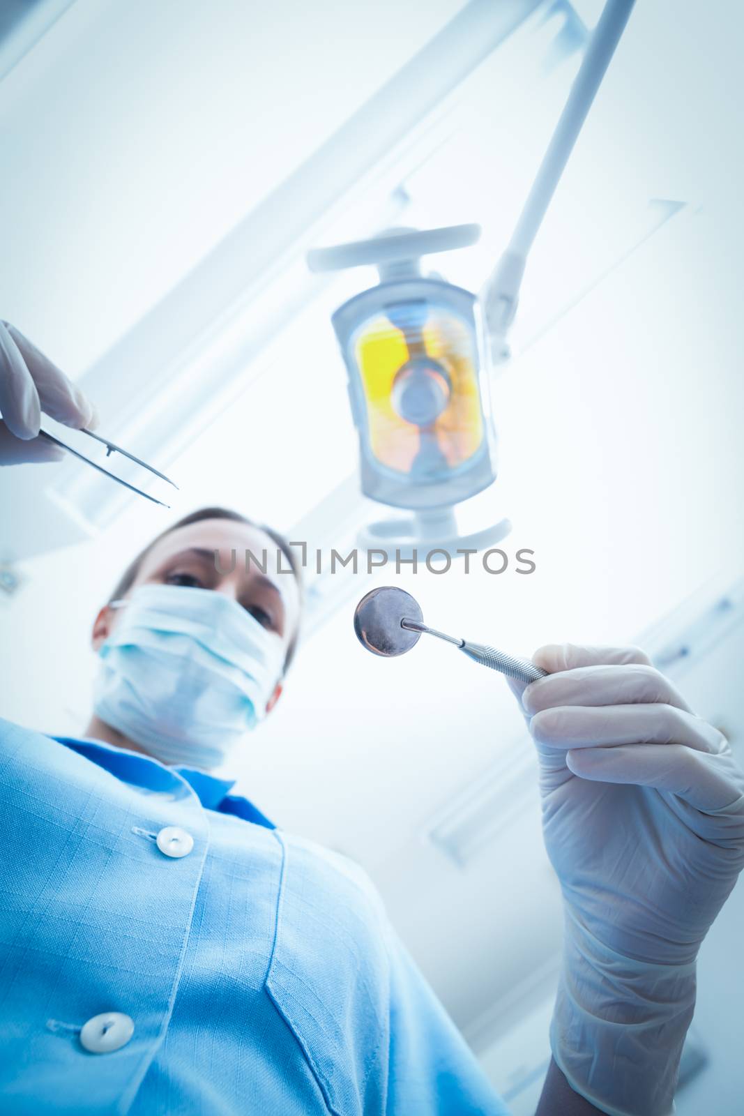 Low angle portrait of female dentist in surgical mask holding dental tools