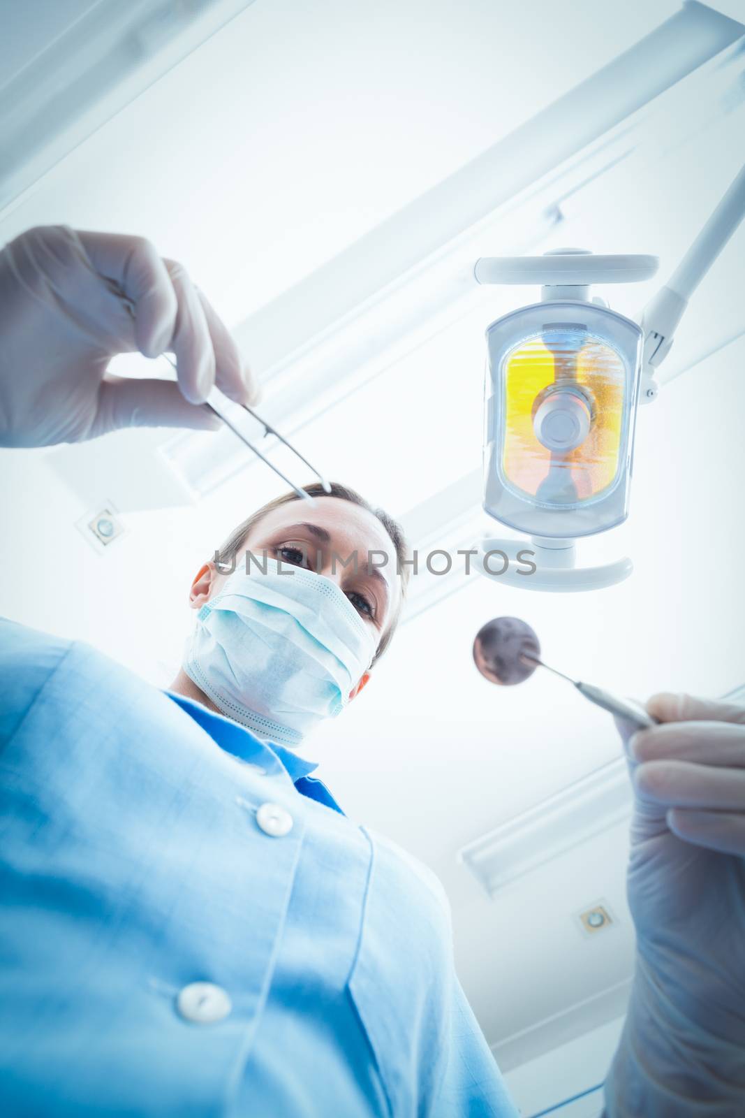 Low angle portrait of female dentist in surgical mask holding dental tools