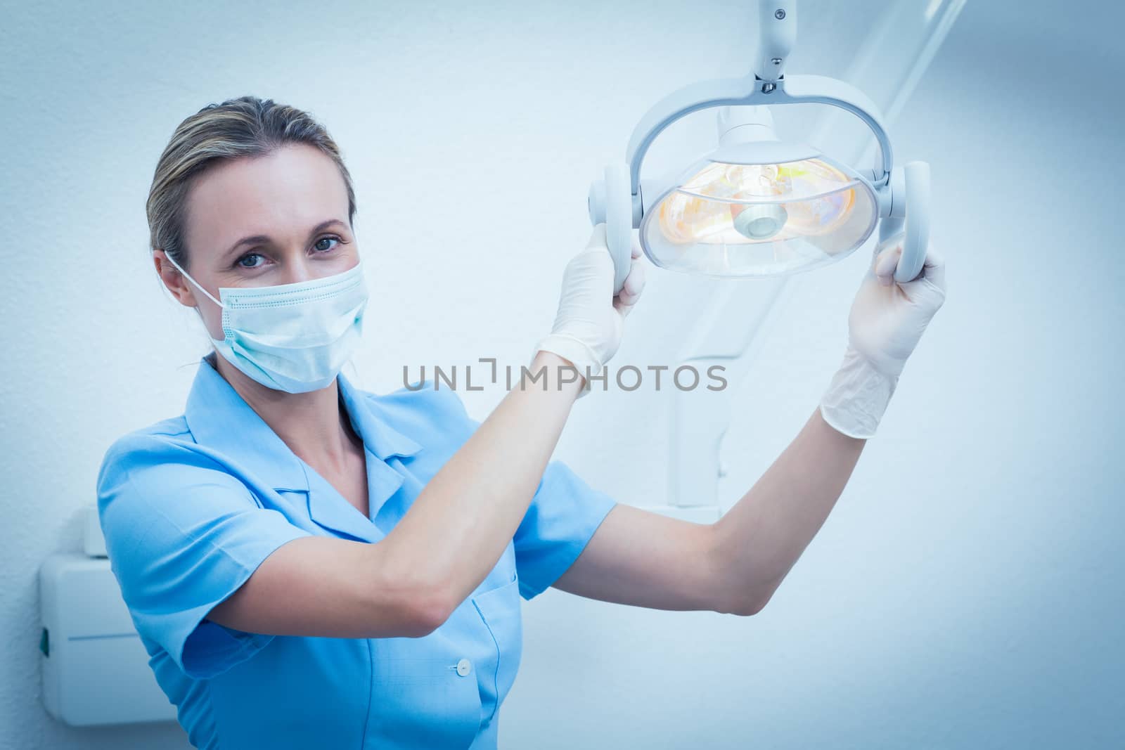 Female dentist in surgical mask adjusting light by Wavebreakmedia