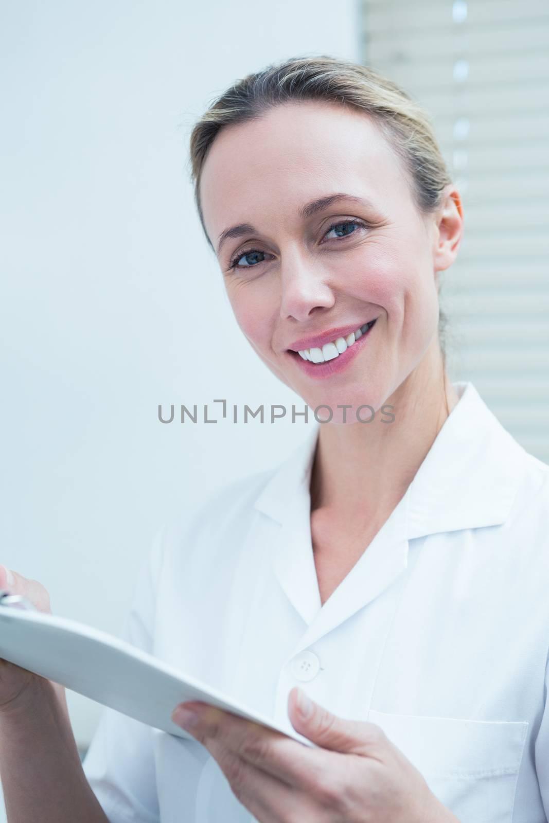 Smiling female dentist holding clipboard by Wavebreakmedia