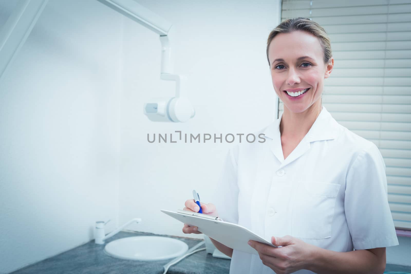 Smiling female dentist holding clipboard by Wavebreakmedia