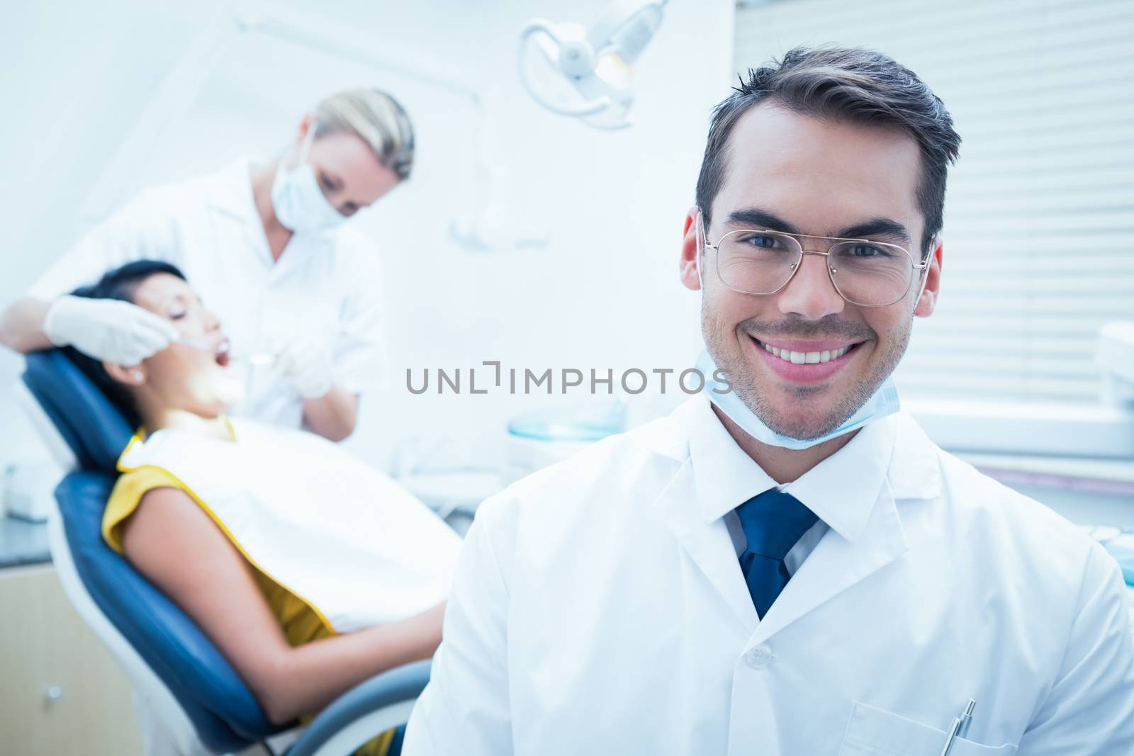 Smiling male dentist with assistant examining womans teeth by Wavebreakmedia
