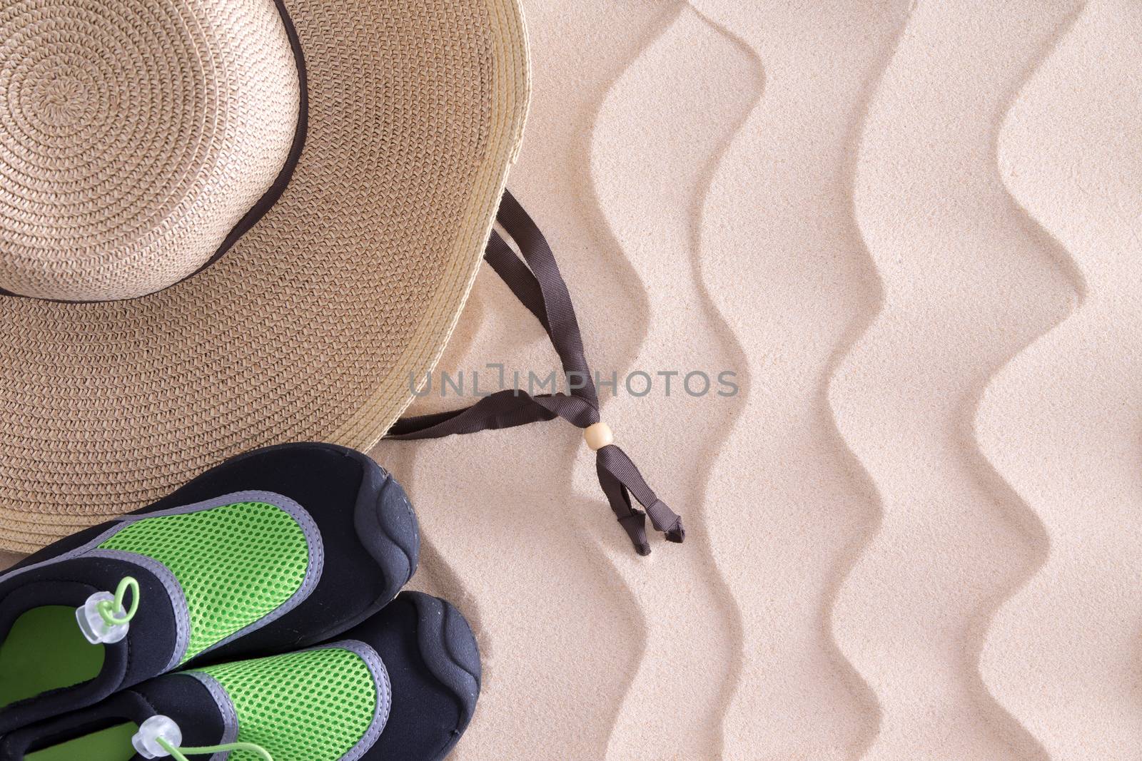 Overhead view of a young boys straw sunhat and green casual shoes on golden sand with a decorative wavy pattern and copyspace on a tropical beach left behind when he went to swim