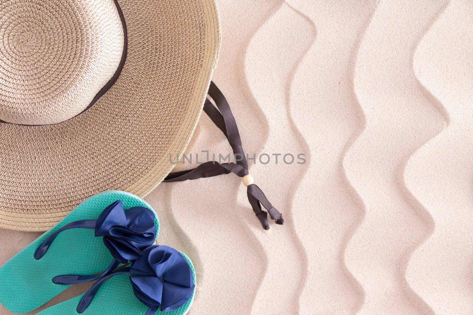 Young girl gone swimming leaving her wide brimmed straw sunhat and slip slops on the golden beach sand with a decorative wavy pattern and copyspace, view from above