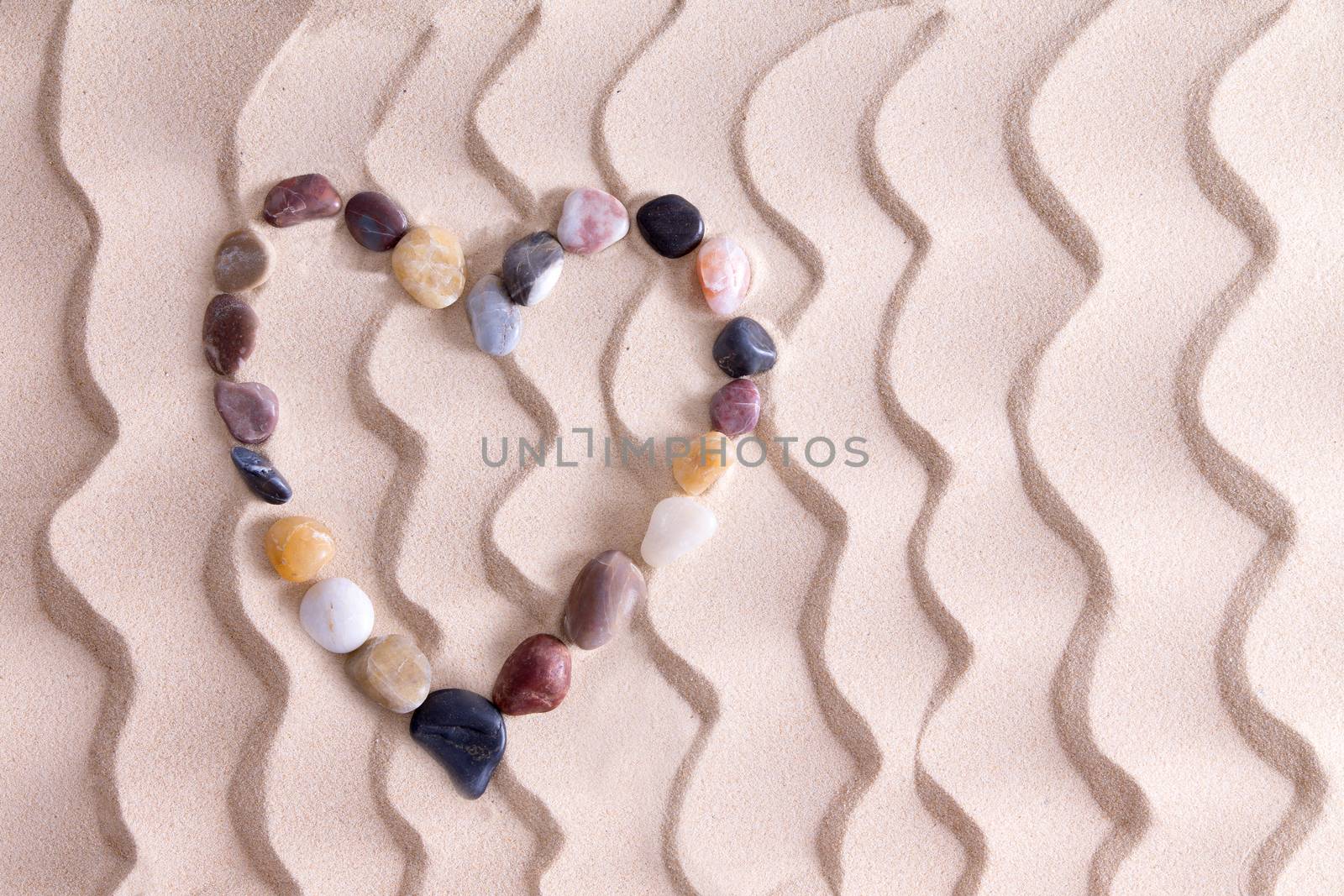 Decorative pebble heart of waterworn alluvial quartzite, agate and basalt stones symbolic of love and romance on golden beach sand with an ornamental pattern of wavy lines and copyspace