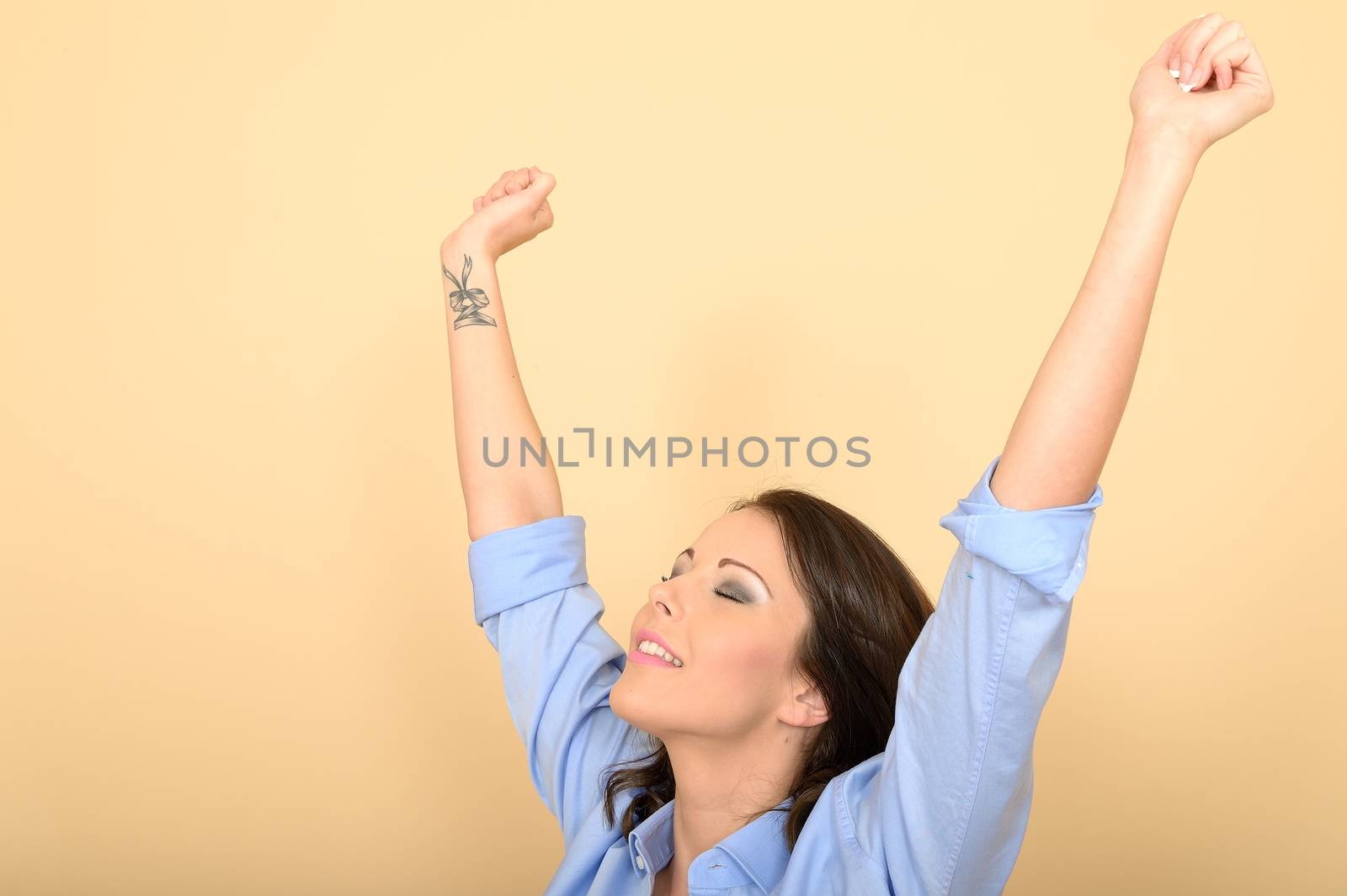 Attractive Young Woman Sitting on the Floor Wearing a Blue Shirt and White Jeans Raising Her Hands in Excitement