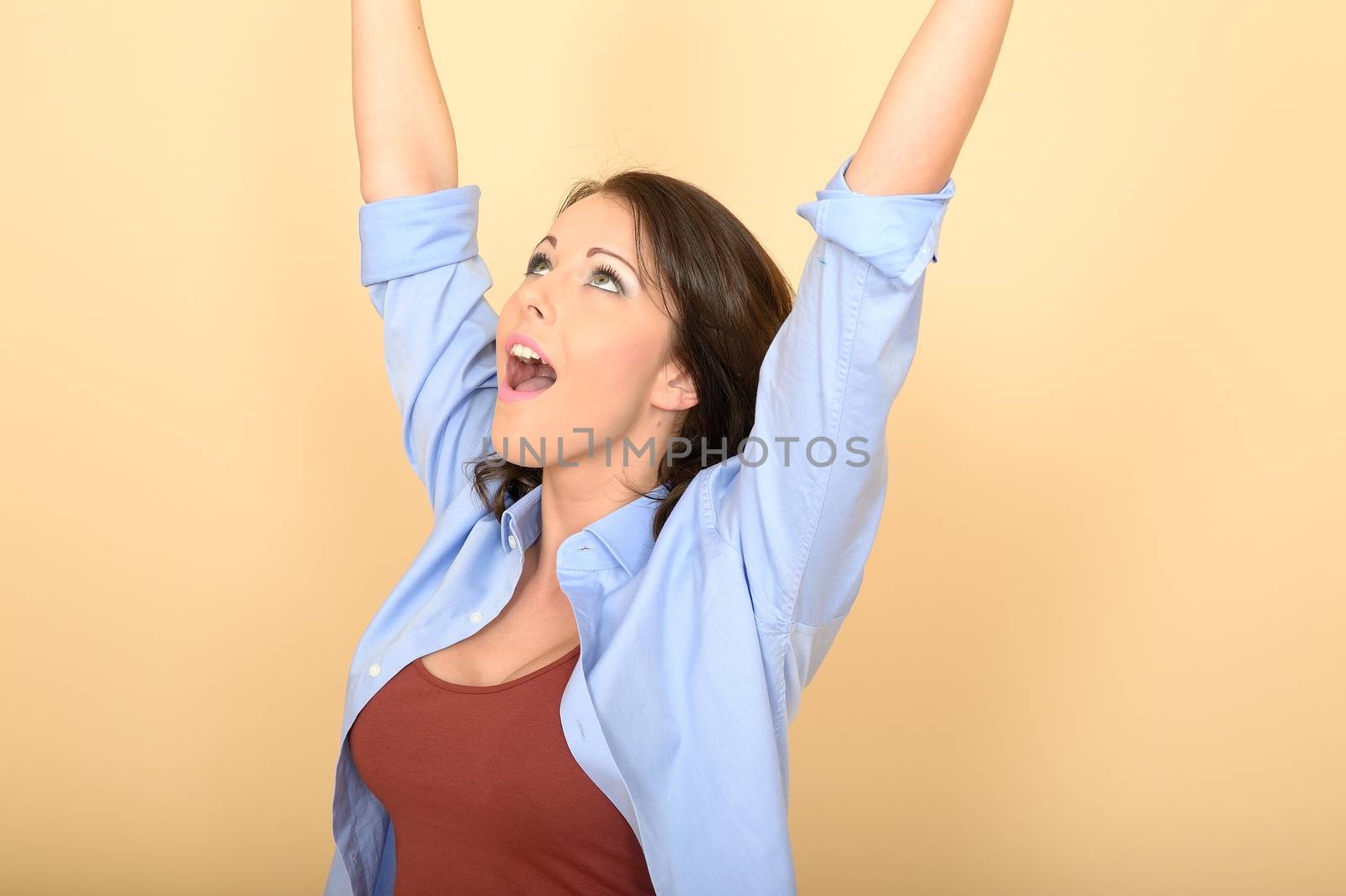 Attractive Young Woman Sitting on the Floor Wearing a Blue Shirt and White Jeans Raising Her Hands in Excitement
