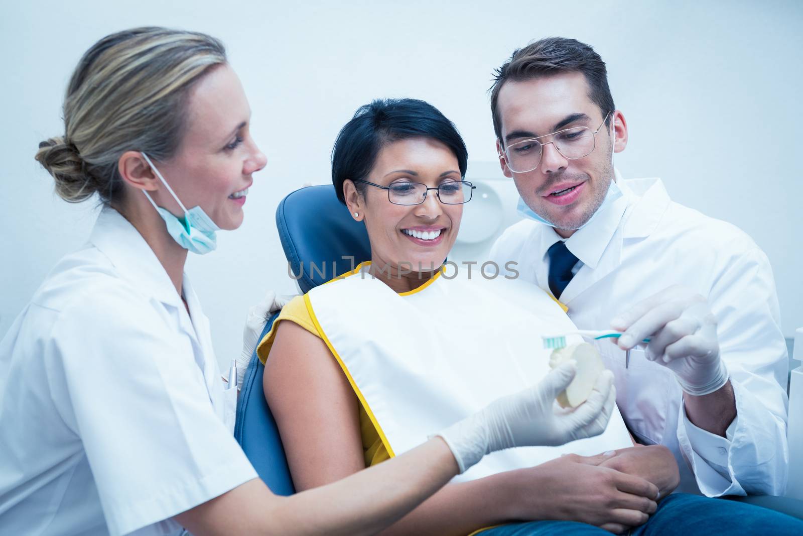 Dentist with assistant showing woman how to brush teeth by Wavebreakmedia