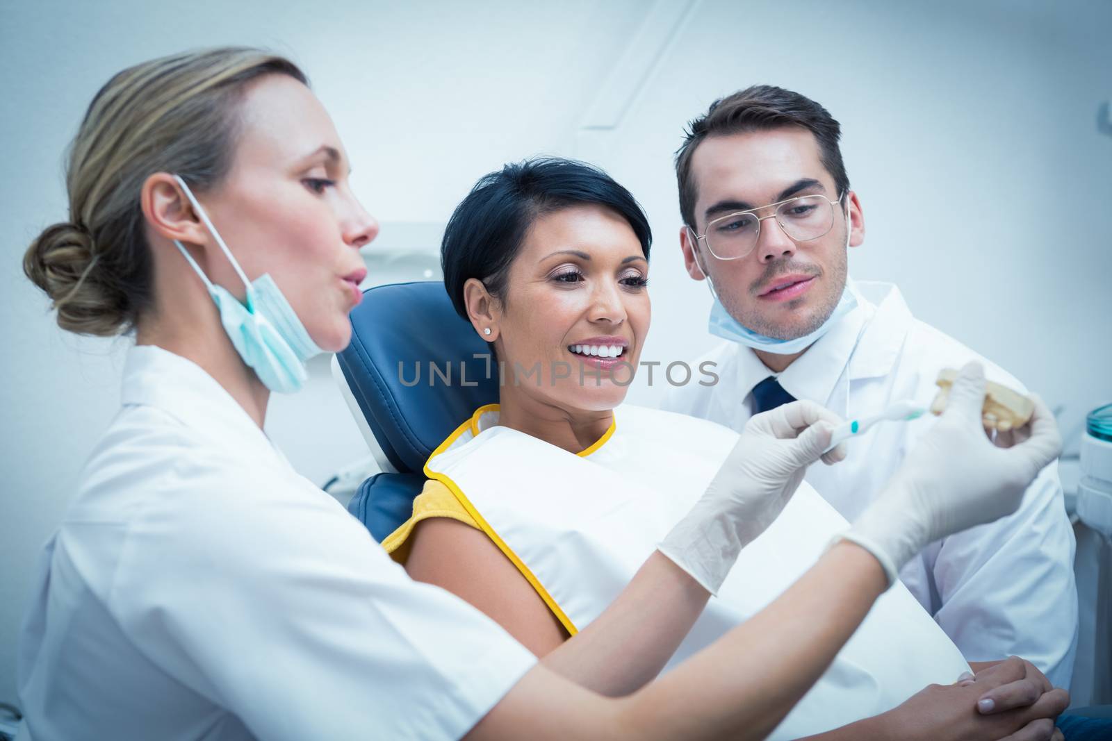 Female dentist with assistant showing woman how to brush teeth in the dentists chair