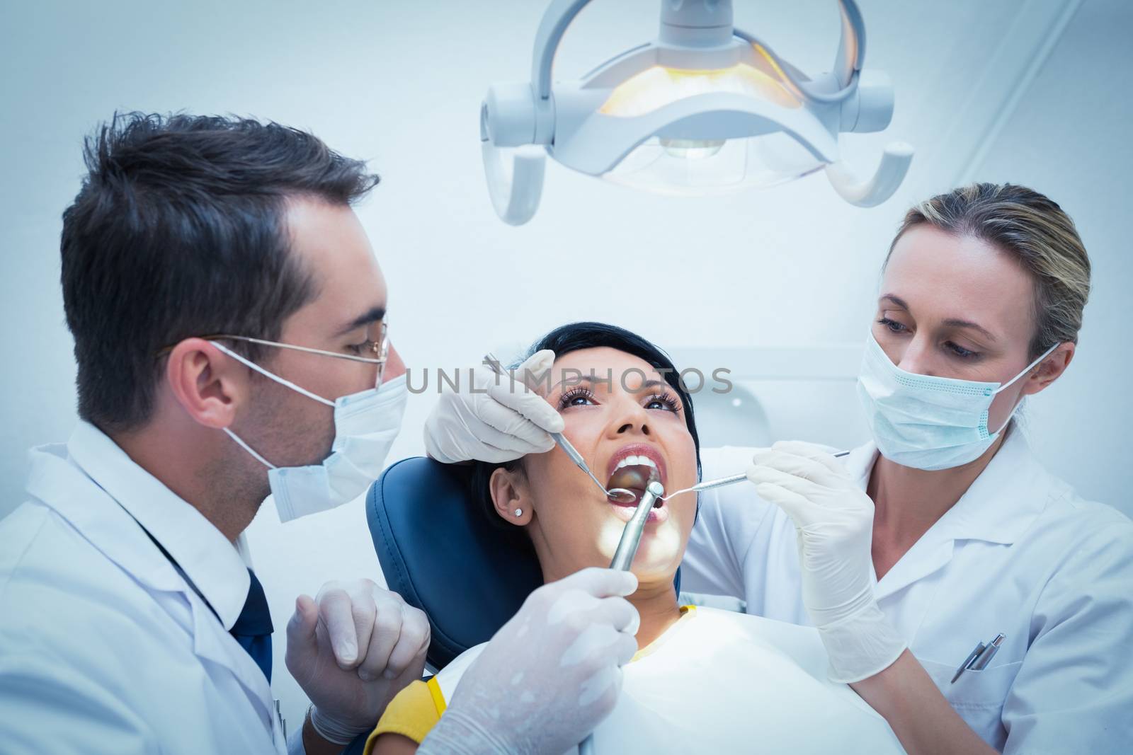 Male dentist with assistant examining womans teeth in the dentists chair