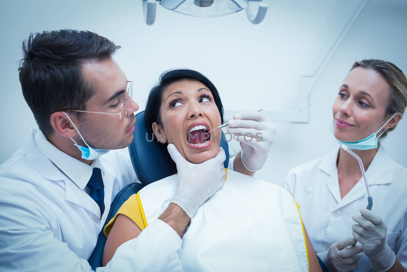 Male dentist with assistant examining womans teeth in the dentists chair