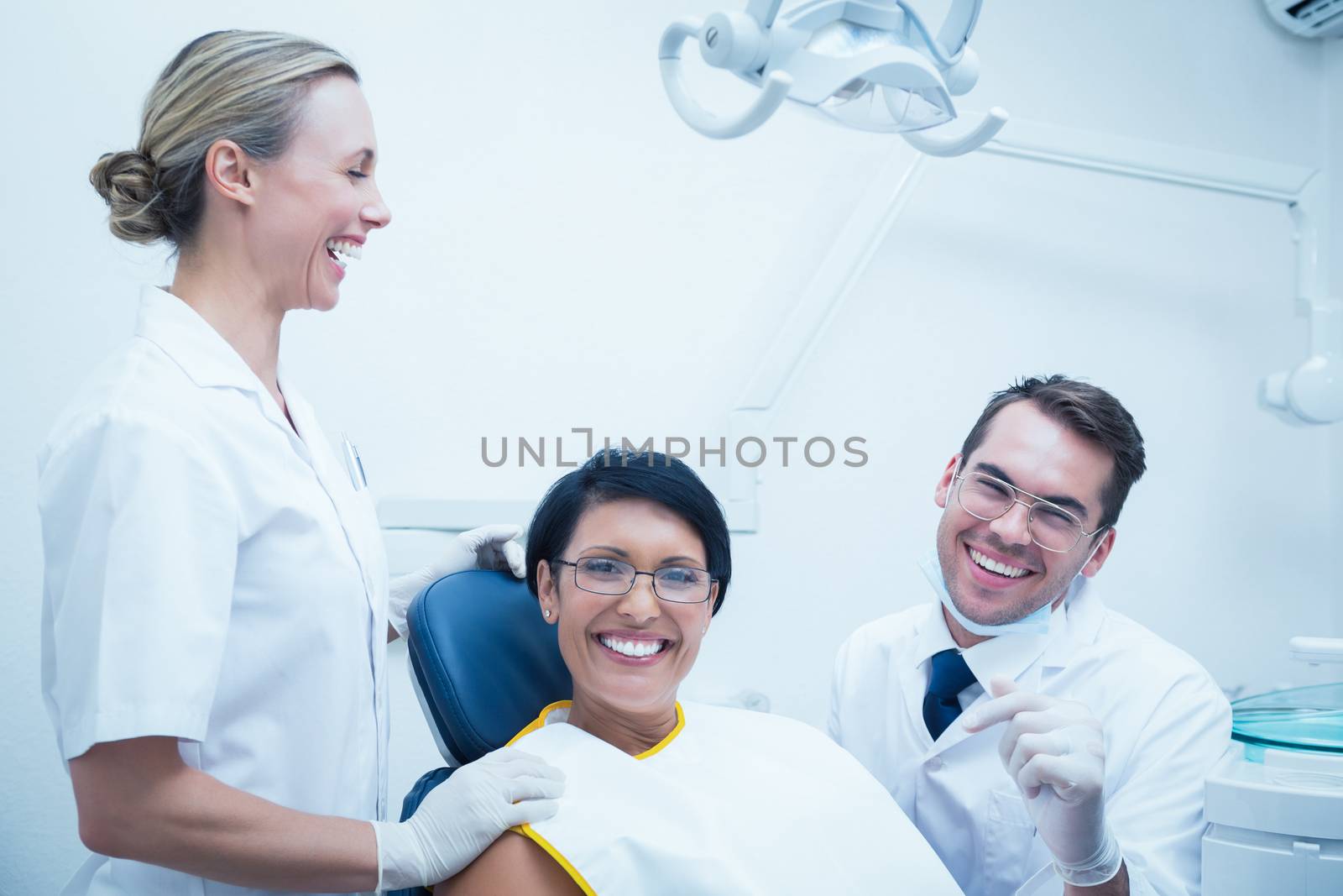 Portrait of cheerful male dentist and assistant with female patient in the dentists chair